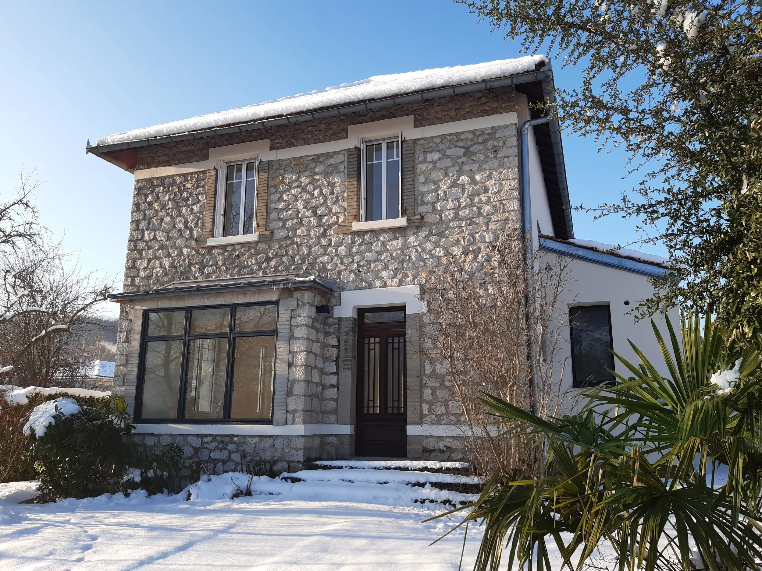Maison en pierre avec deux fenêtres à volets blancs et bow window.