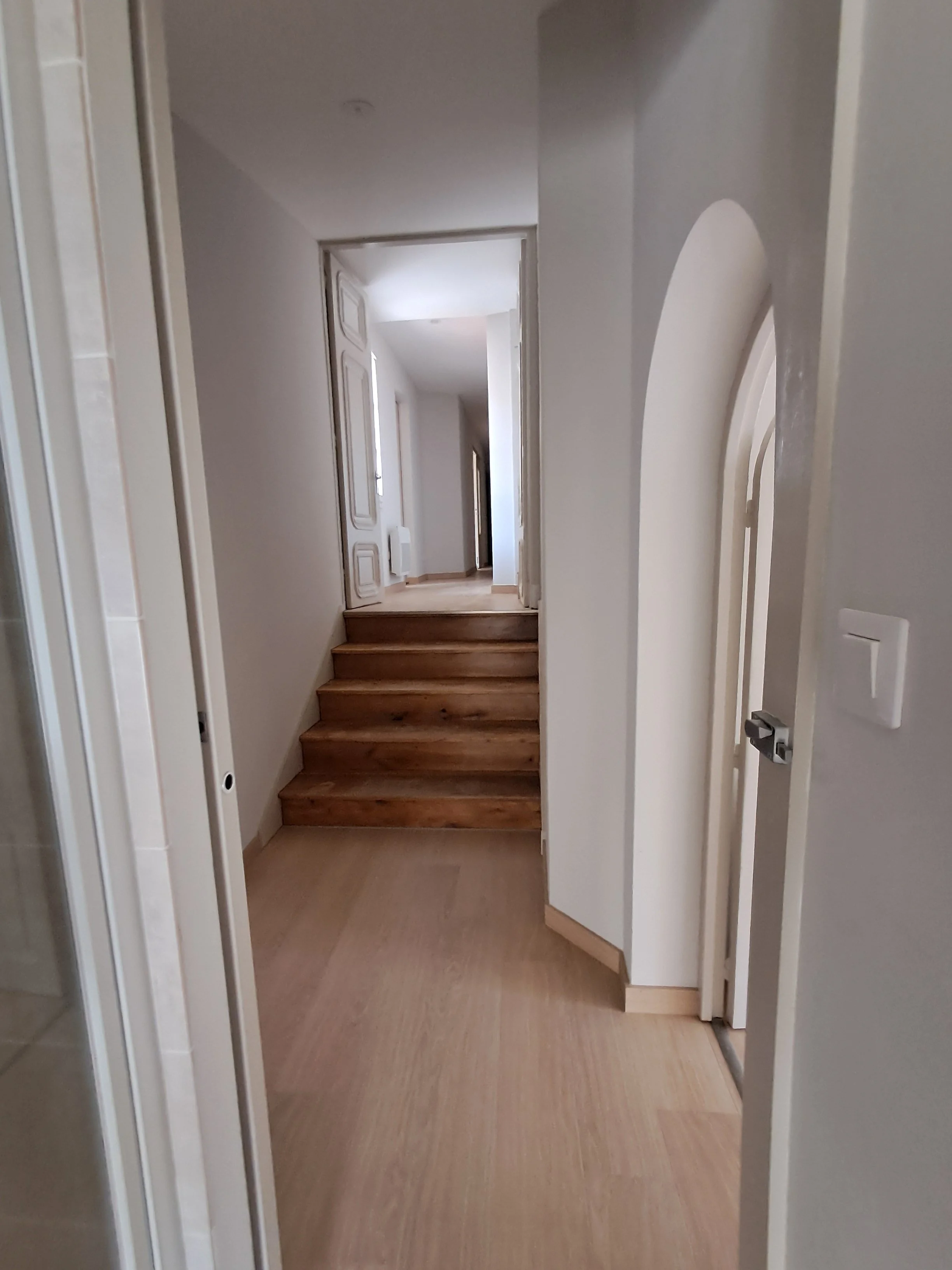 Hall d'entrée avec escalier en bois menant à un autre étage et murs blancs.
