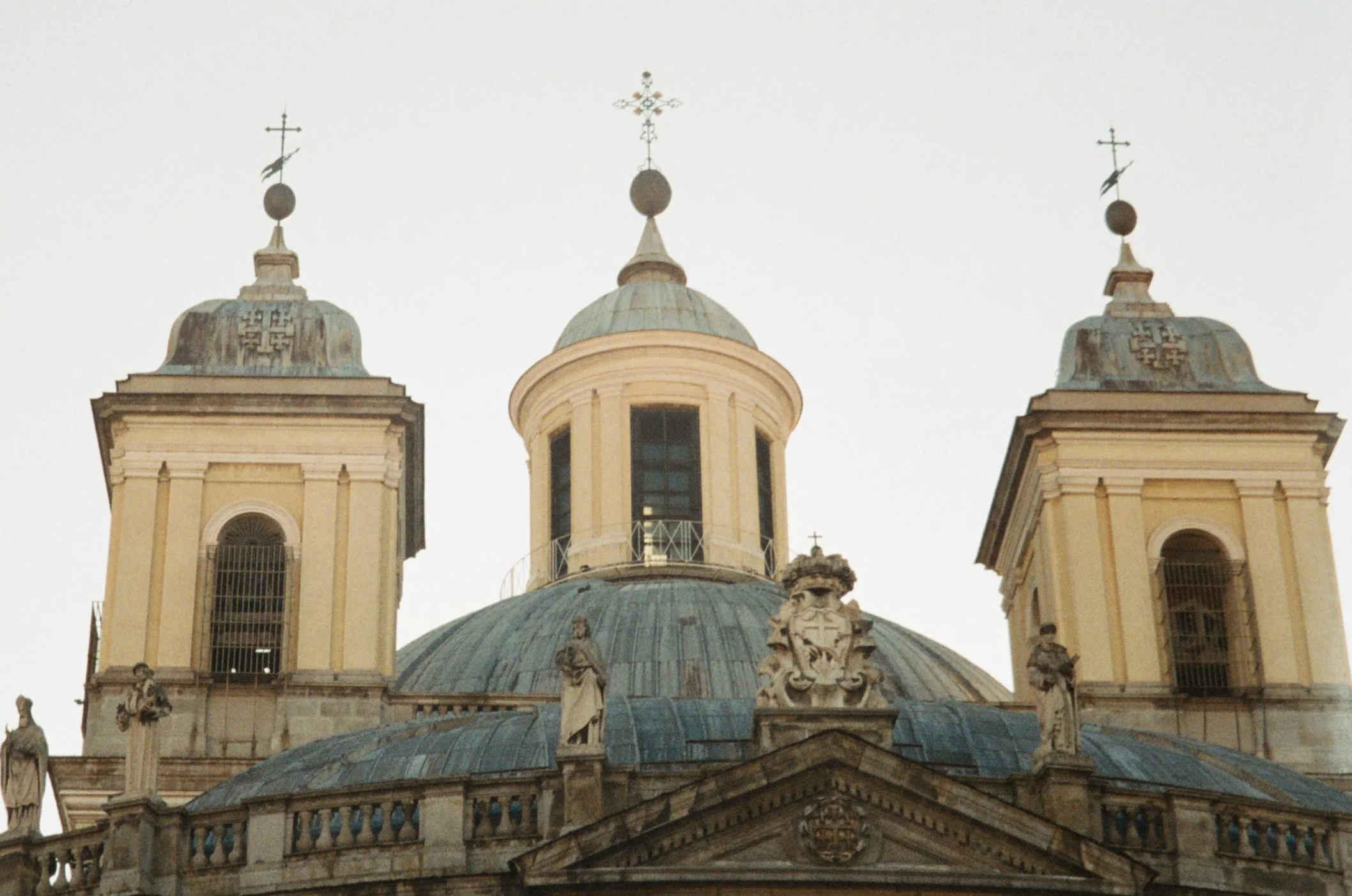 View of an ornate historic church with two tall towers and a central dome, adorned with crosses and decorative statues.