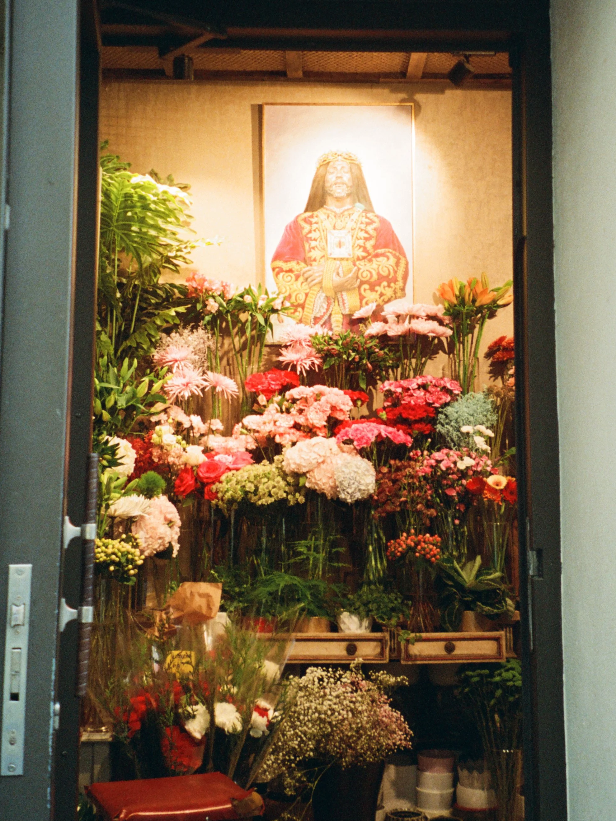 A religious altar with a large portrait of Jesus Christ surrounded by various colorful flowers and plants.