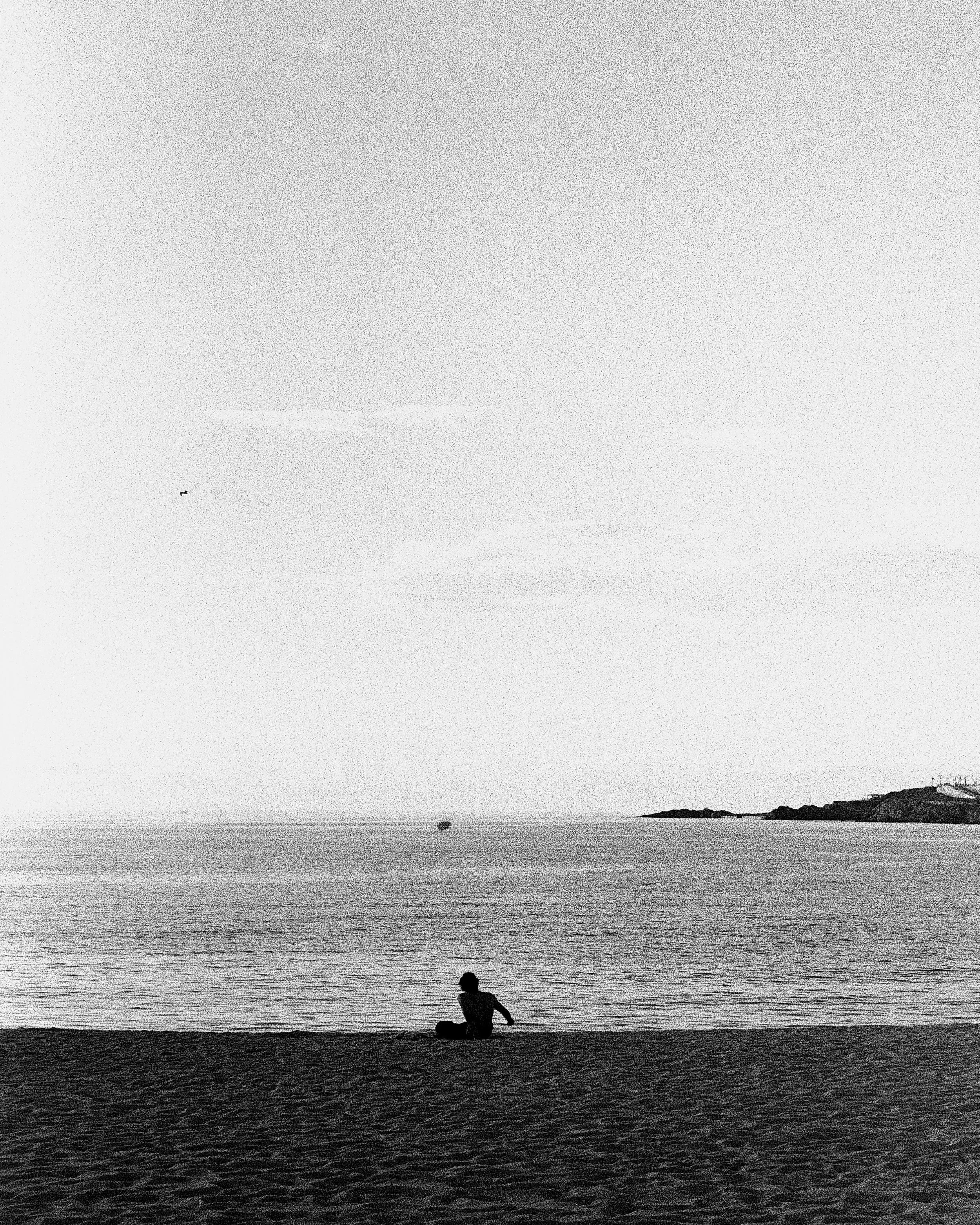 Silhouette of a child playing near the shoreline with a calm sea and islands in the background during sunset or dusk.