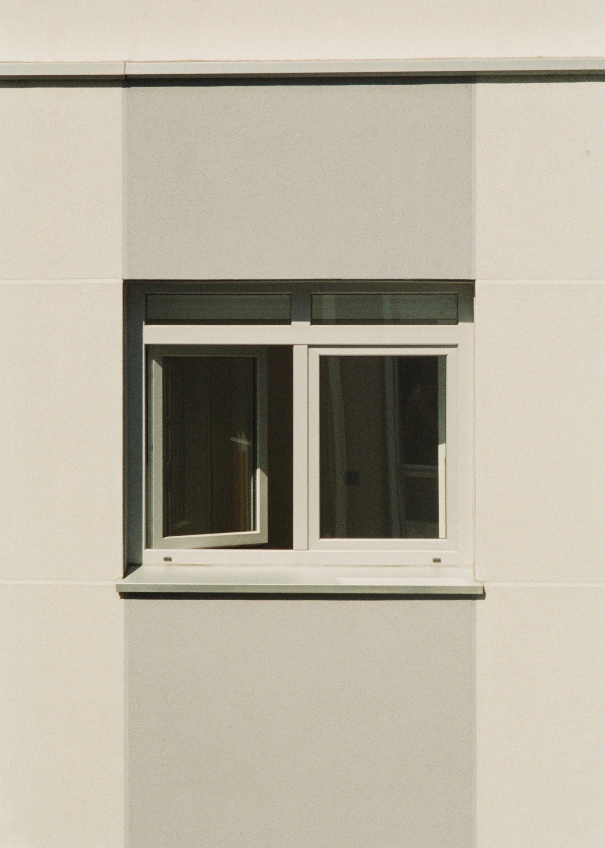 A white window with a sliding pane wall with a gray trim. The window is set into a flat, white exterior wall.