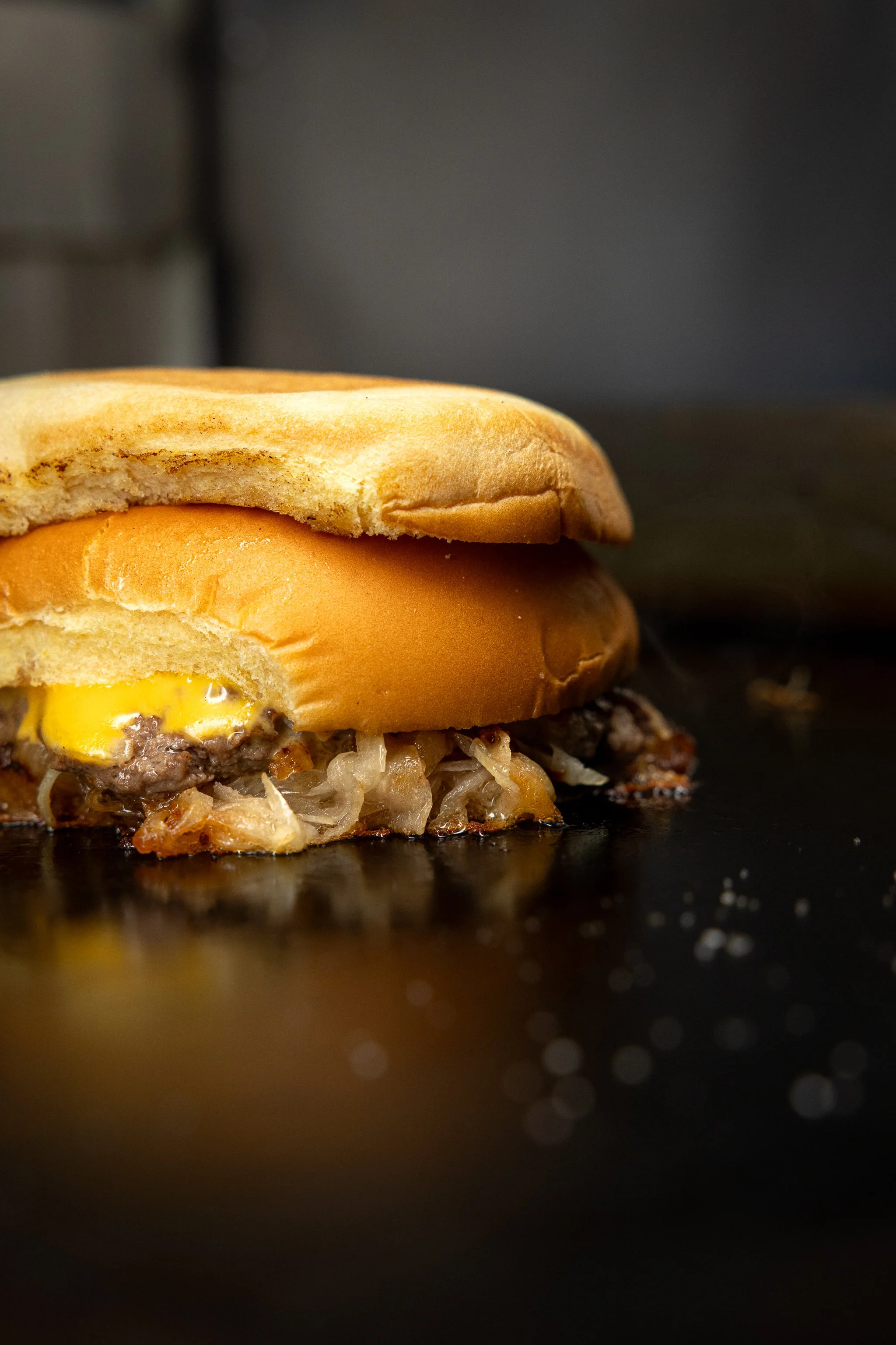 Ein Hamburger mit Rindfleischpatty, Cheddar-Käse, Zwiebeln, auf einem schwarzen Hintergrund.