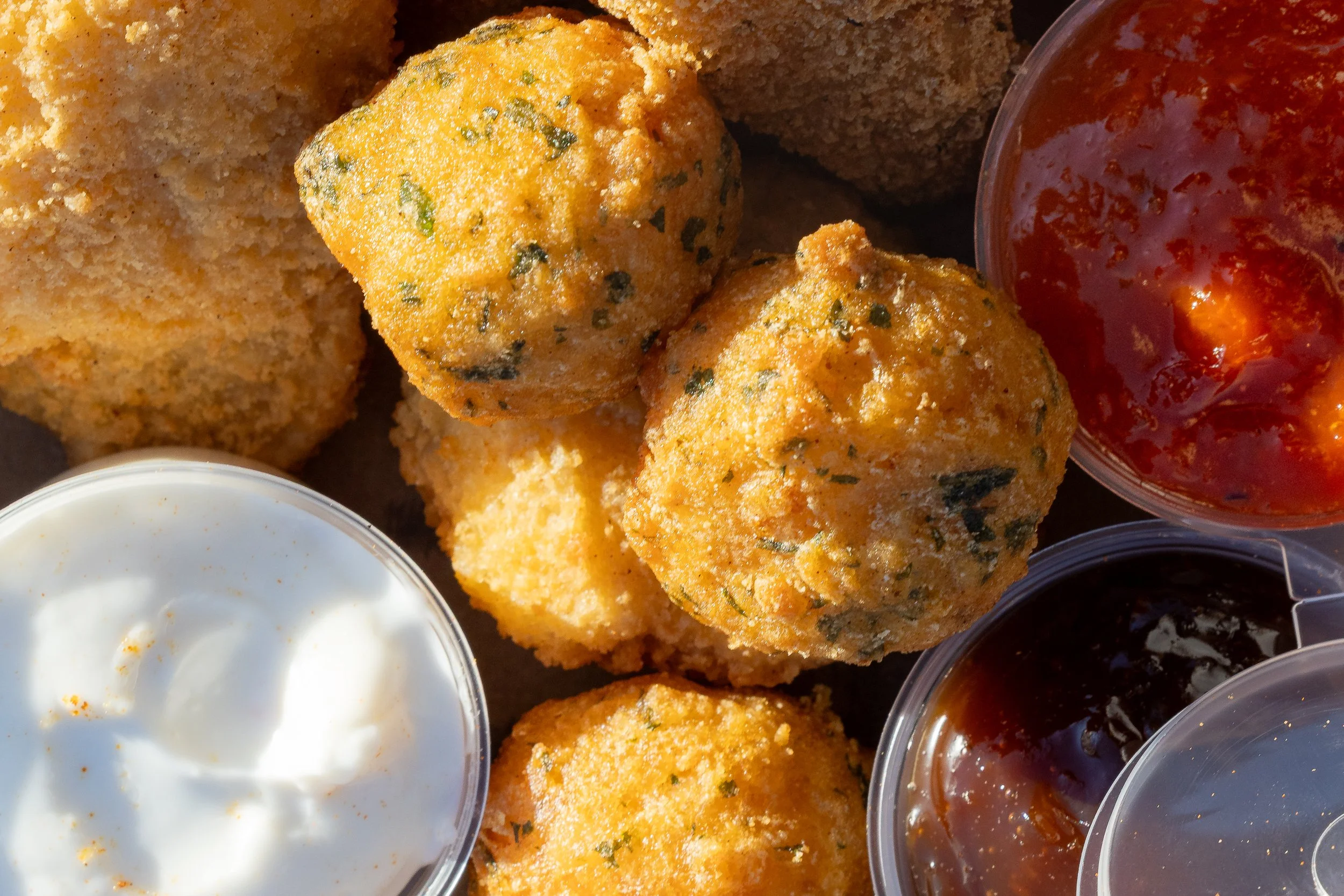 Frittierte Kroketten mit verschiedenen Dips, darunter Sour Cream, Tomatensoße und dunkle Soße.