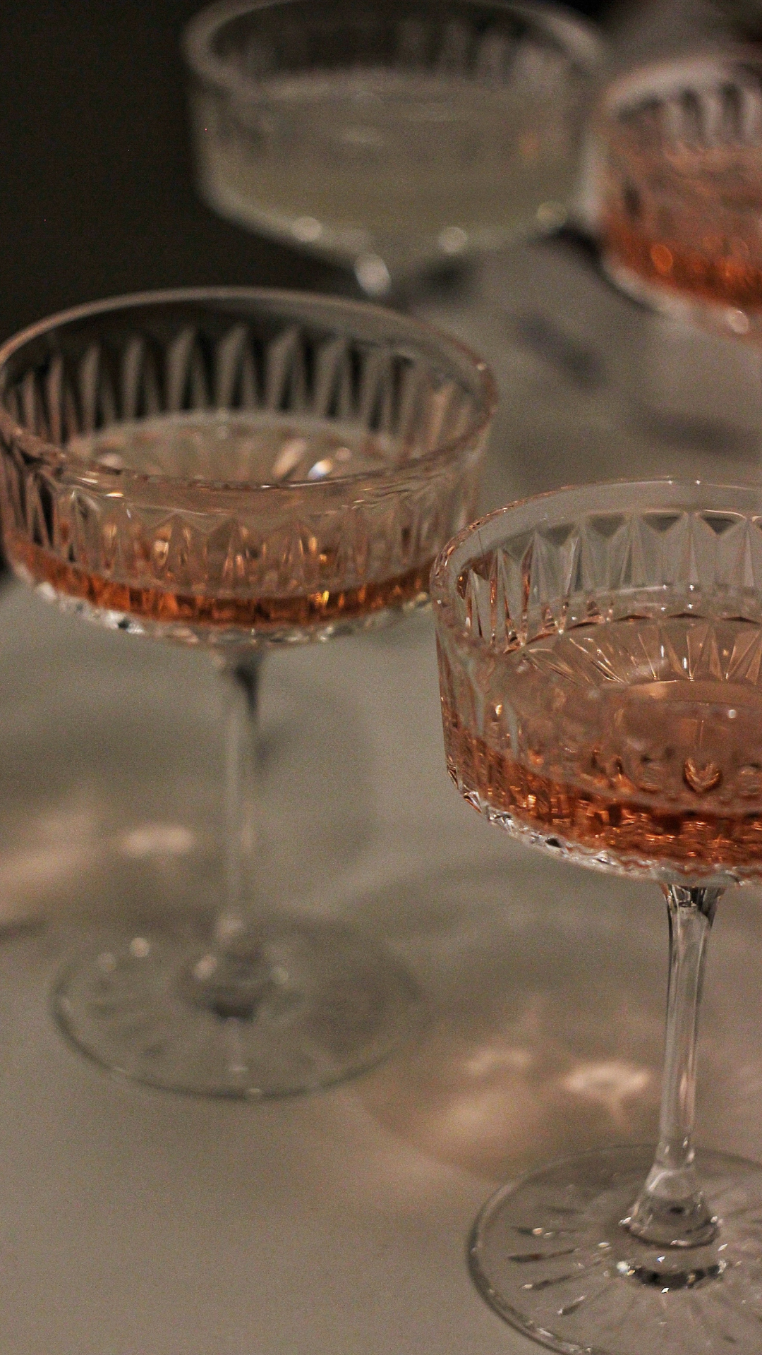 Three crystal champagne glasses filled with pink bubbly liquid on a white surface with a dark background.