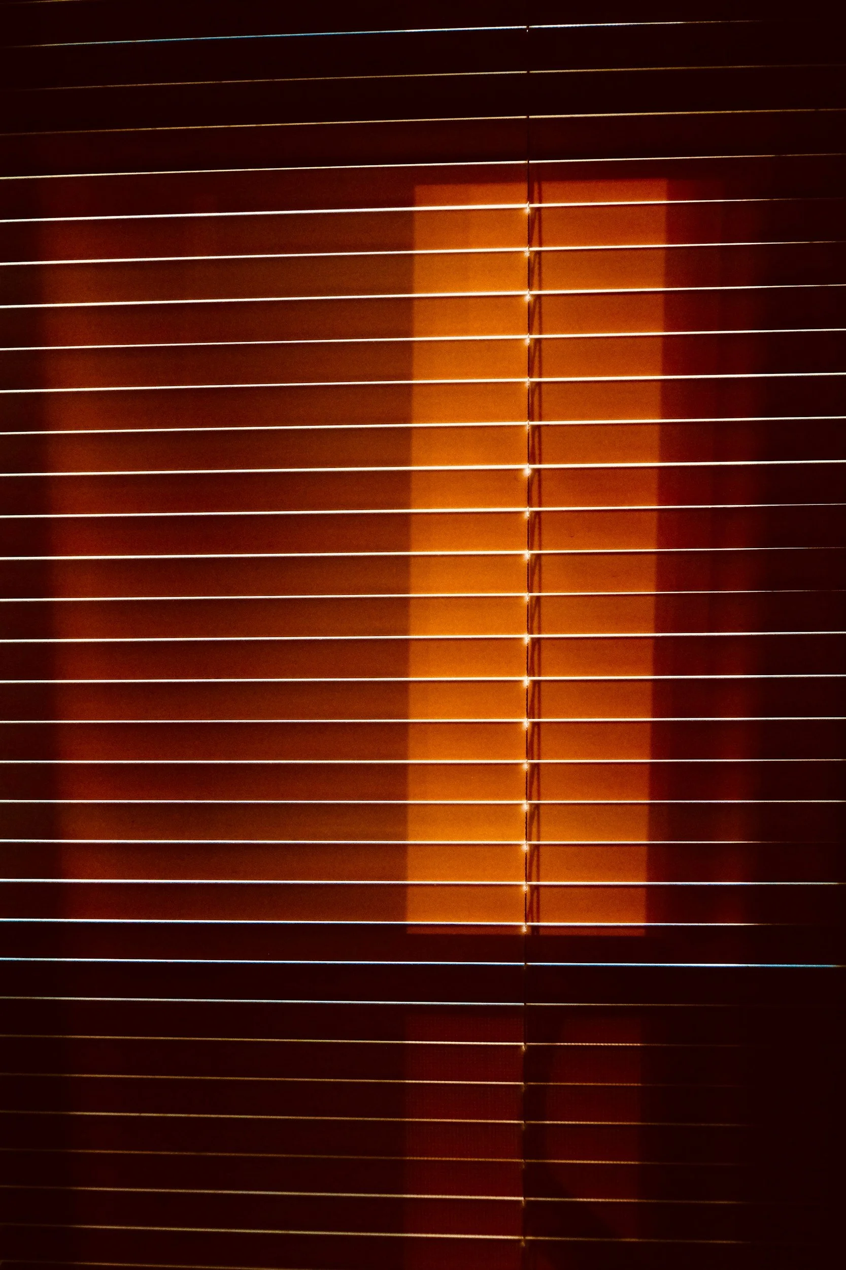 Sunlight shining through wooden window blinds, creating a pattern of light and shadow.