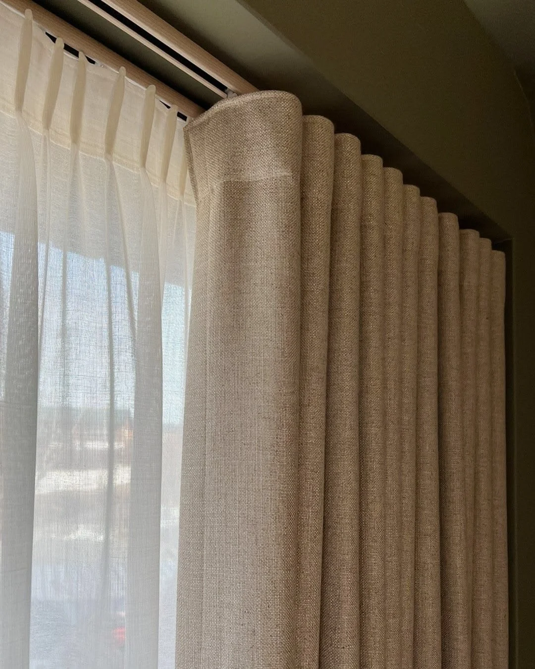 A beige curtain next to a sheer white curtain hanging in front of a window.