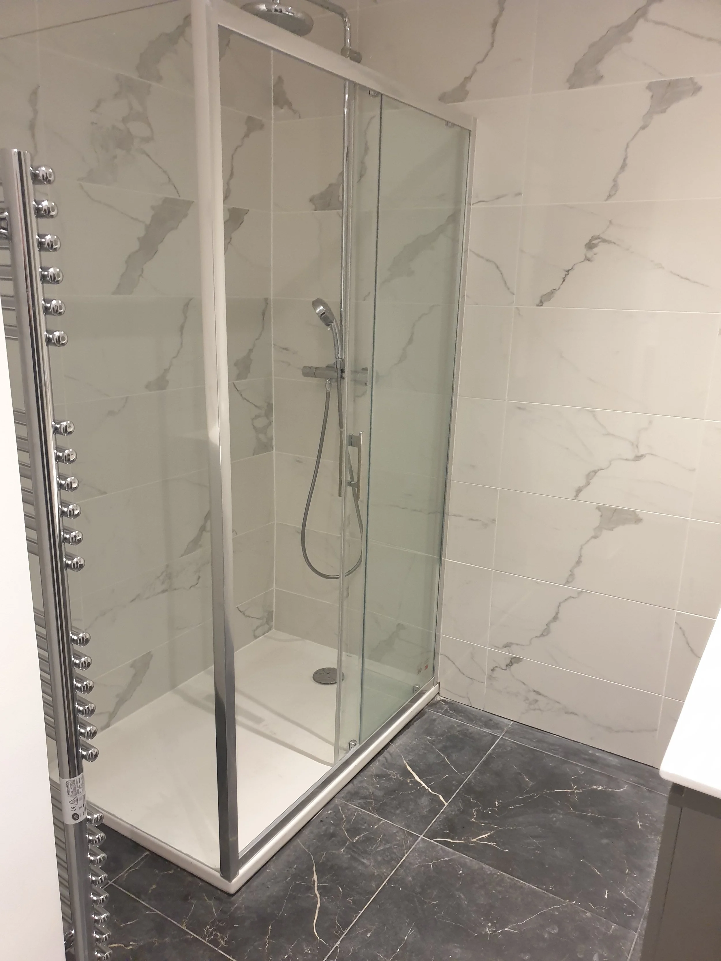 Une cabine de douche moderne avec des murs en marbre blanc et gris, une porte en verre et un plancher en marbre noir avec des veines blanches.