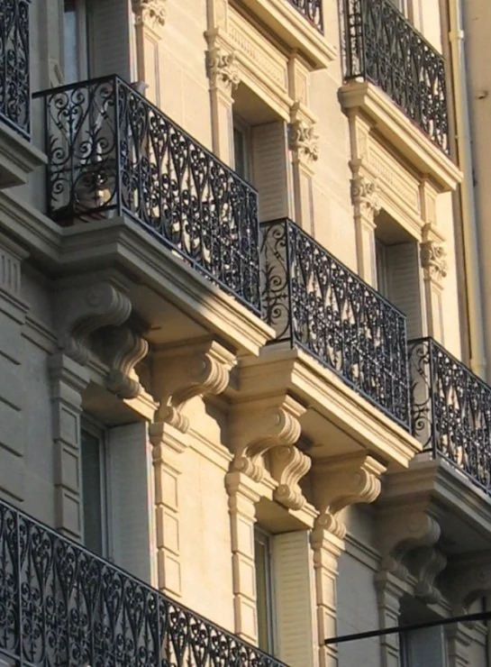 Façade d'un bâtiment avec balcons en fer forgé noir ornés de détails décoratifs et fenêtres à volets blancs dans un style architectural classique