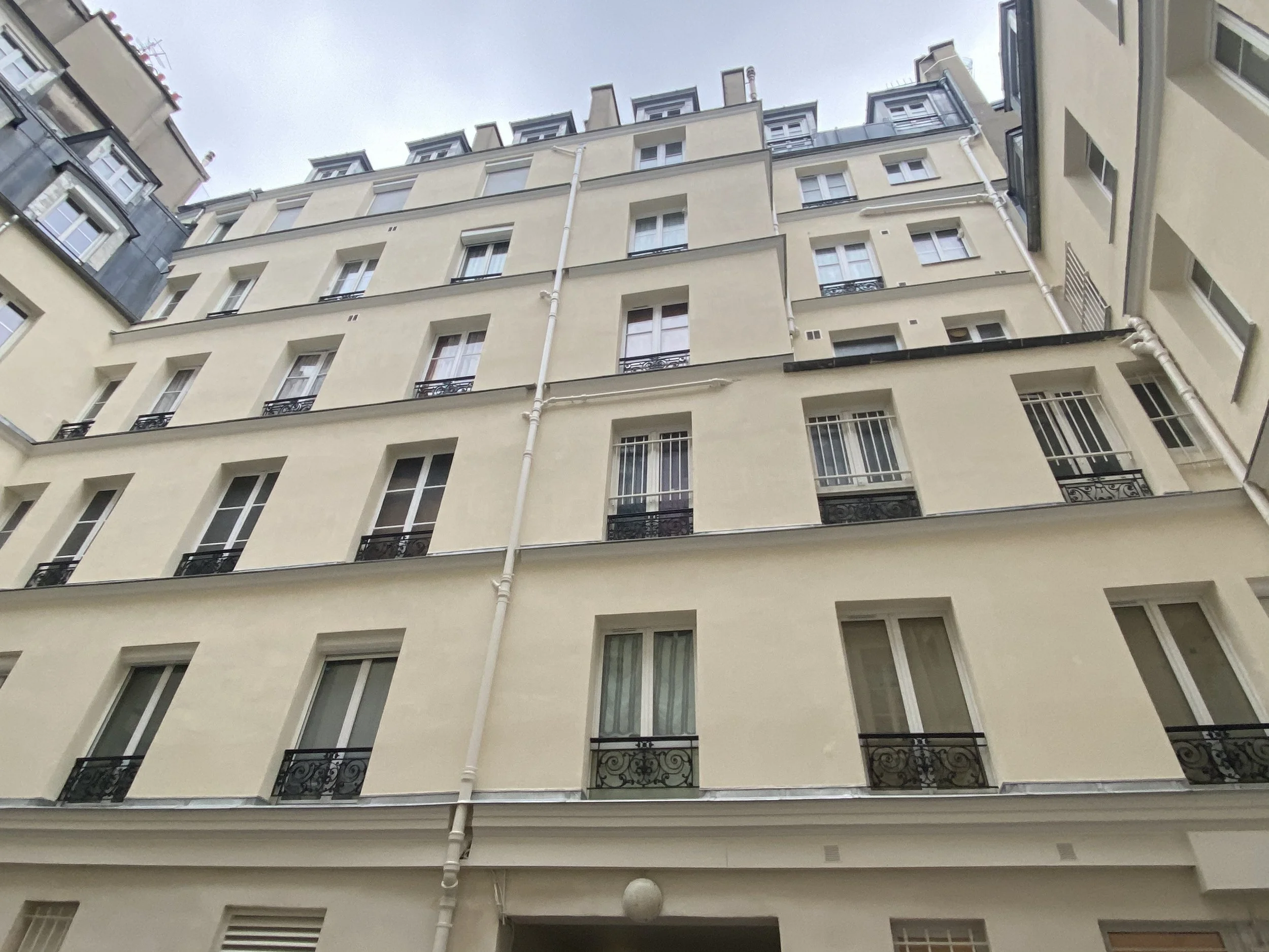 Vue d'un immeuble résidentiel blanc avec plusieurs fenêtres et balcons en fer forgé, vu depuis le bas vers le haut, sous un ciel gris.