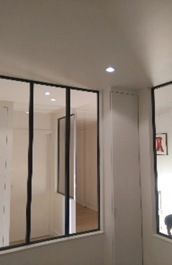 Mur avec miroir et portes en verre séparant deux pièces.
