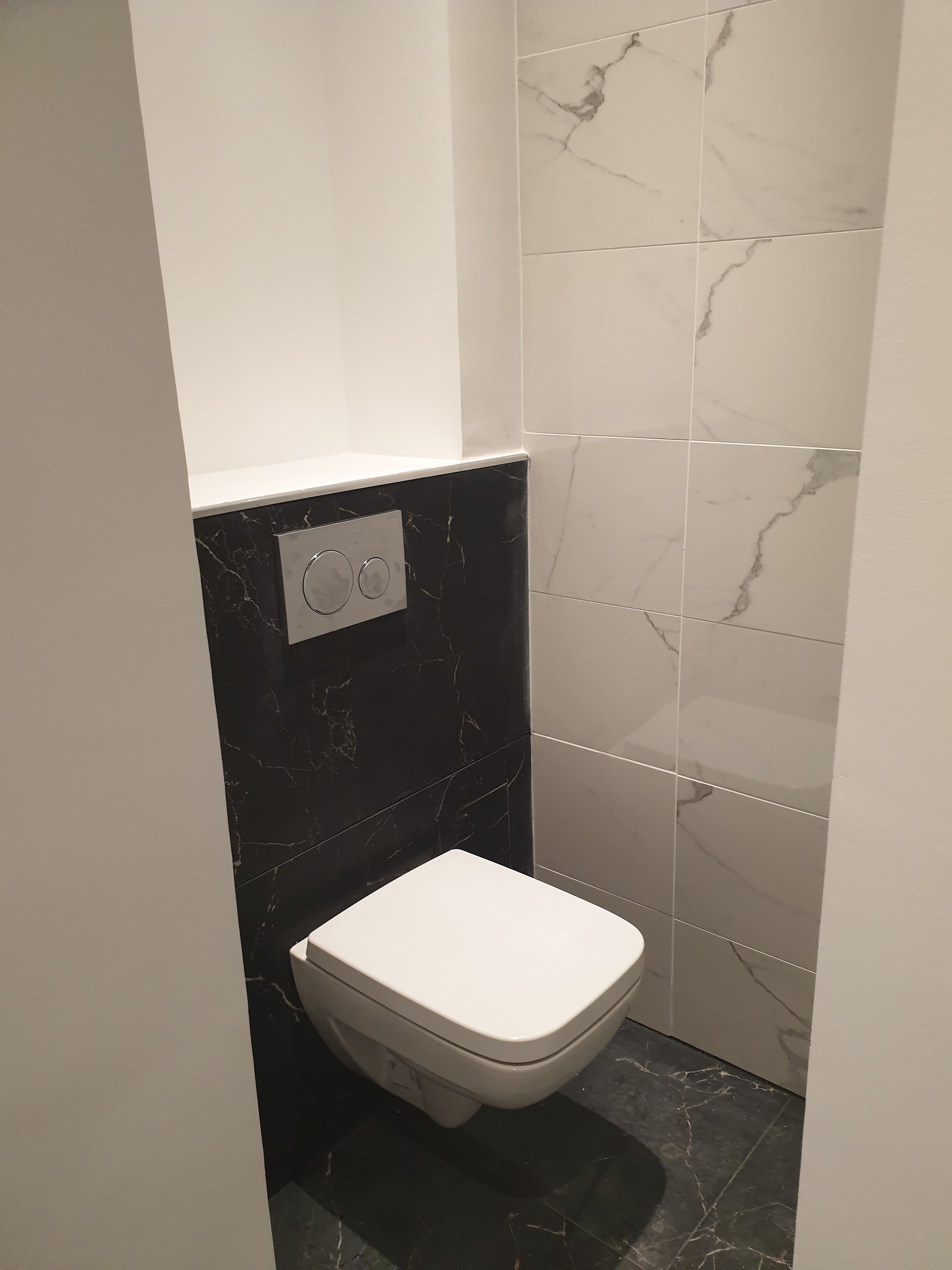 Toilettes modernes dans une salle de bain avec des murs en marbre clair et un lave-mains en marbre noir.