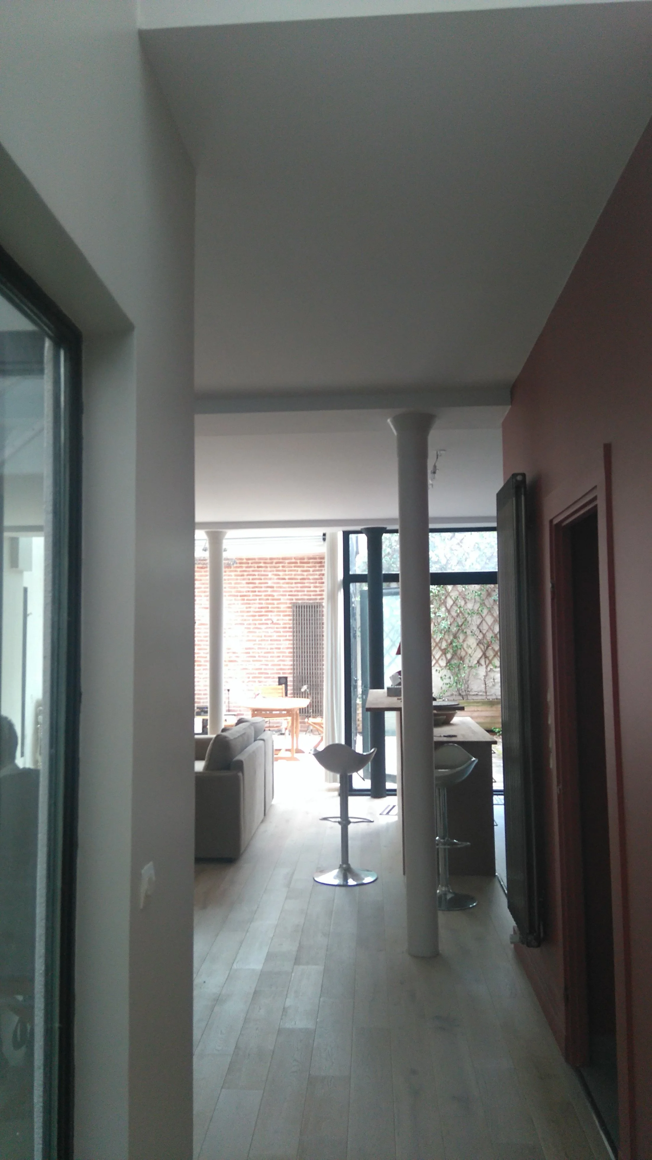Intérieur d'une maison avec un salon et une cuisine ouverte, grandes fenêtres laissant entrer de la lumière.