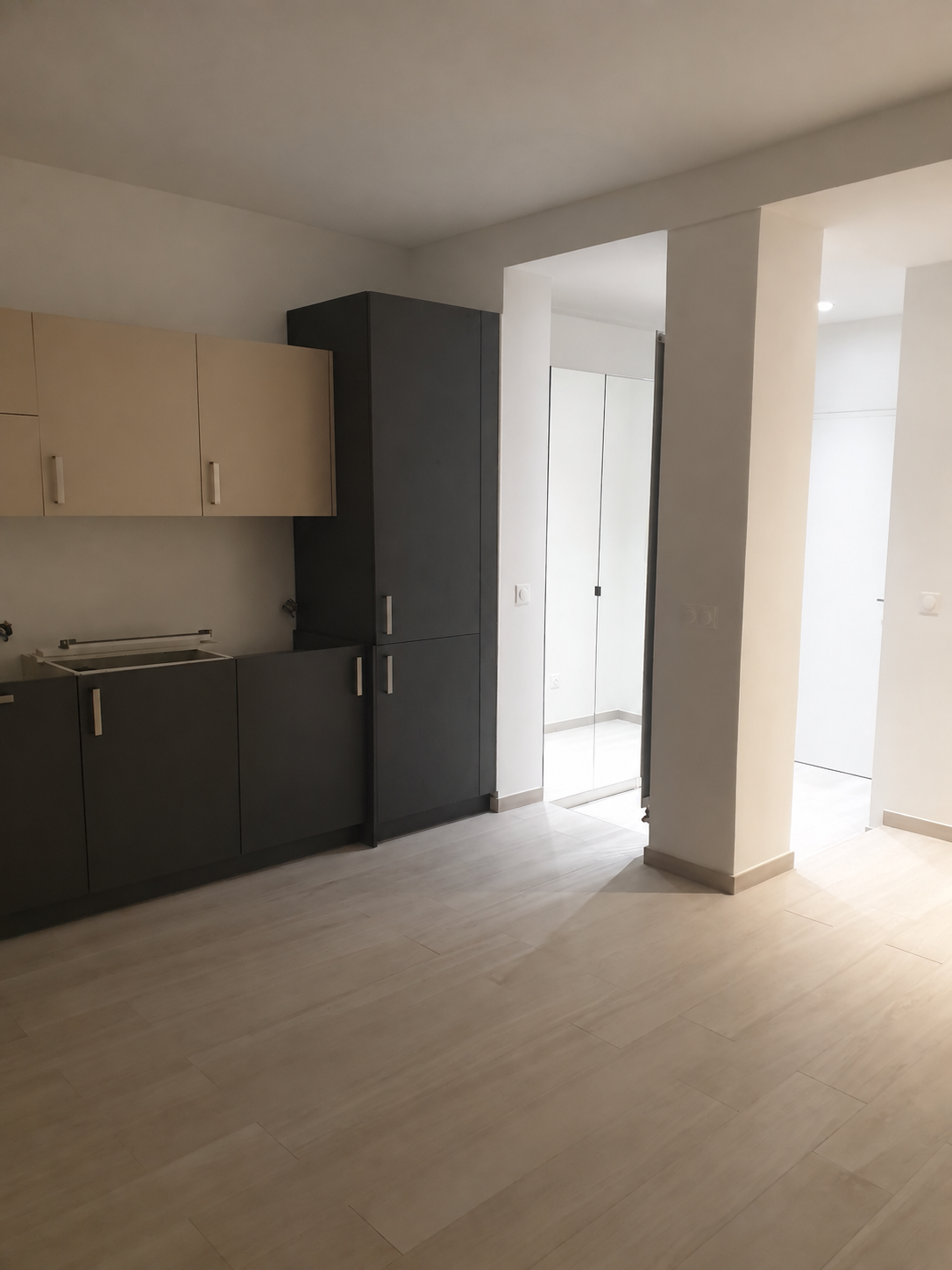 Cuisine moderne avec des armoires noir et beige, sol en bois clair, espace lumineux.