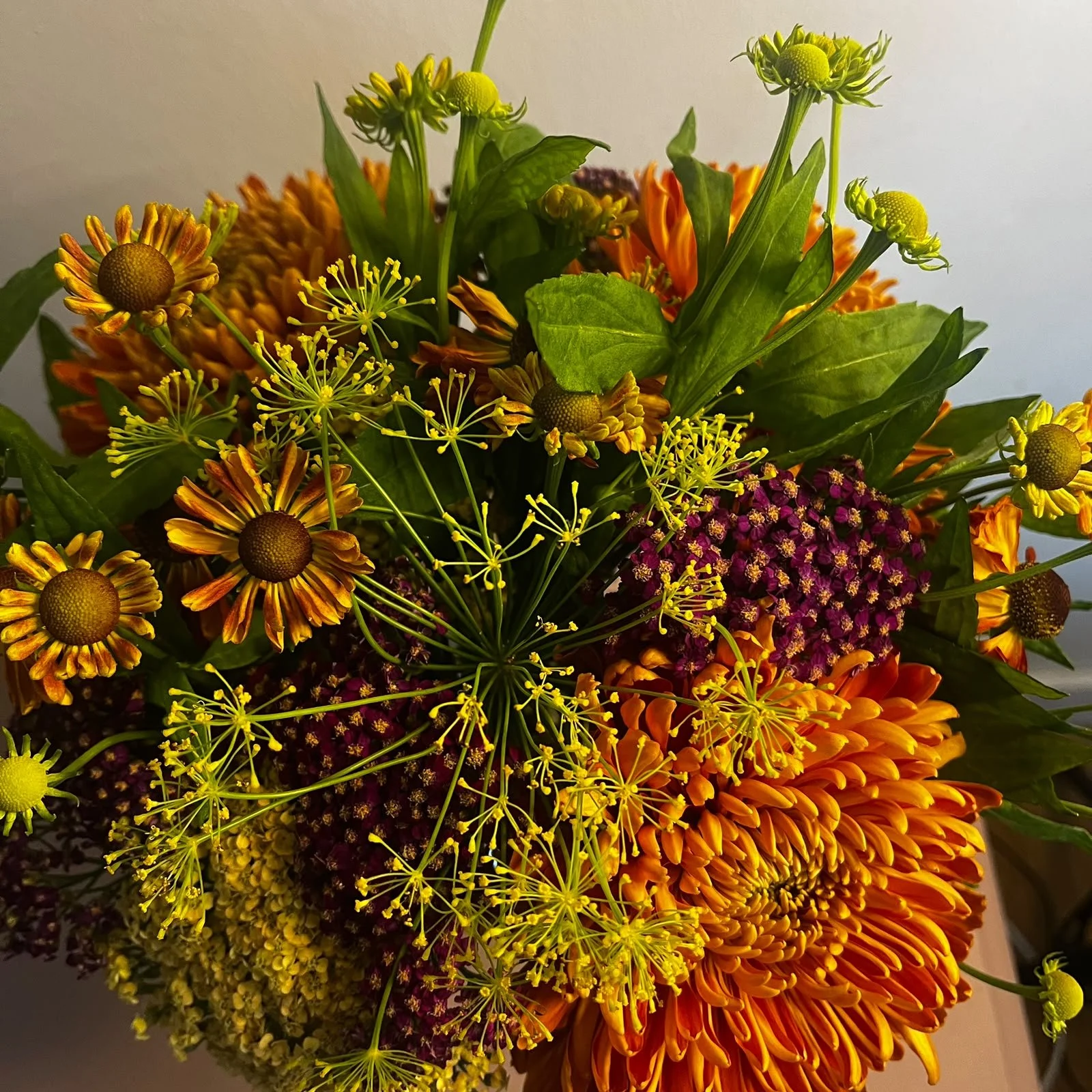 Close-up bouquet of orange chrysanthemums, yellow dill flowers, burgundy filler flowers, and green foliage