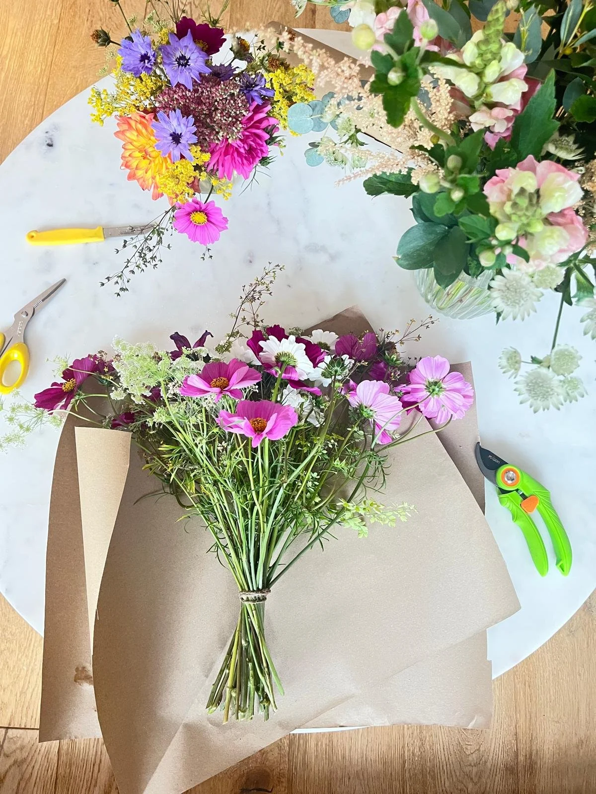 Colorful hand-tied flower bouquet on wrapping paper surrounded by floral arranging tools and loose flowers