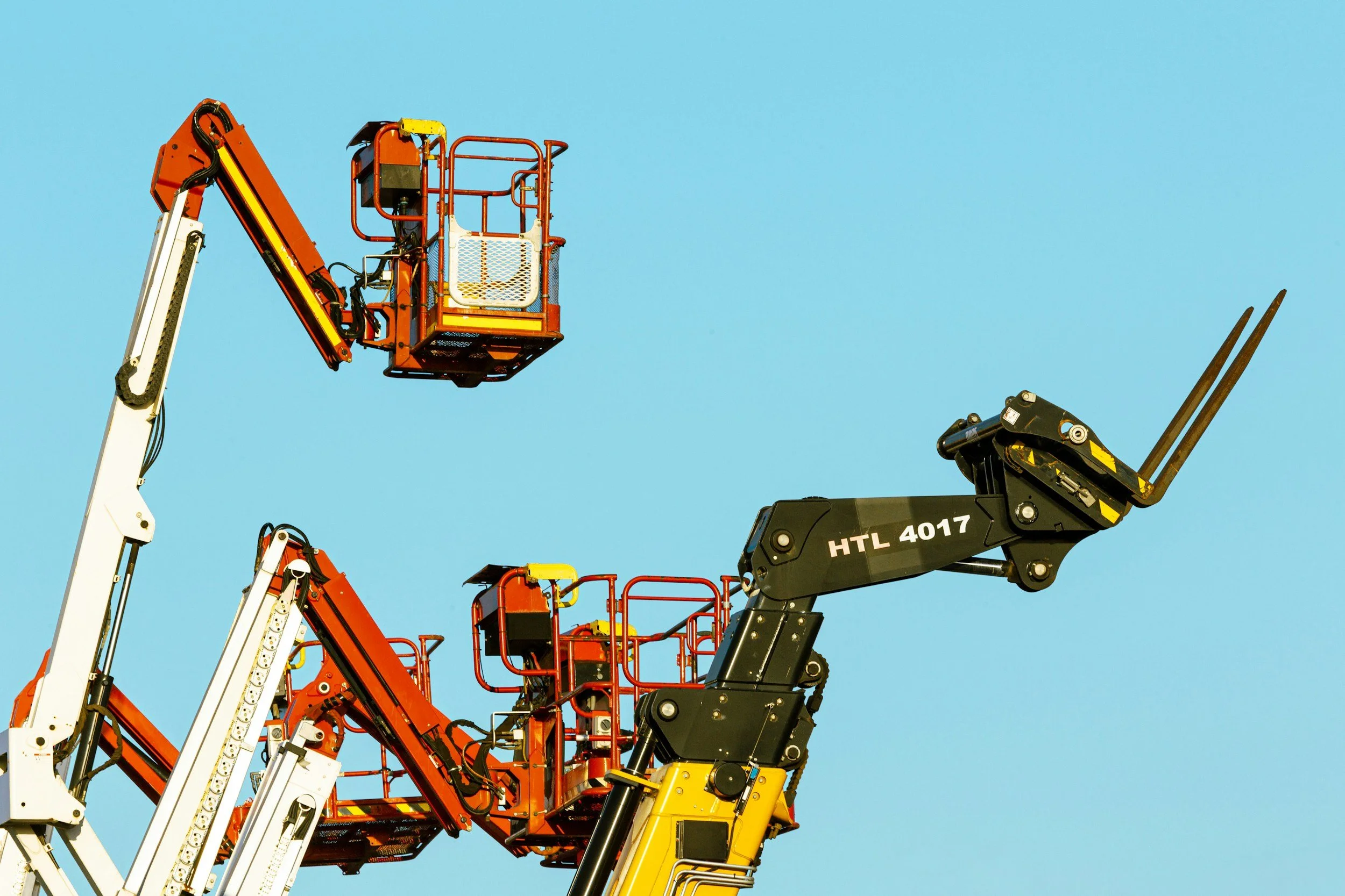 Cherry picker boom lifts raised against a blue sky