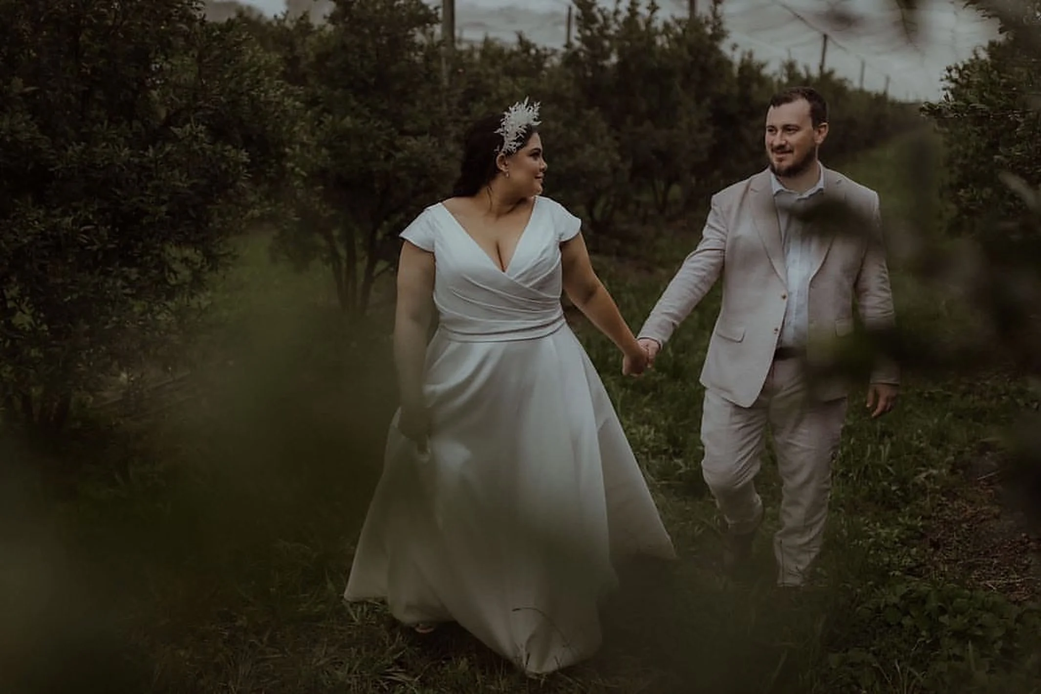 A bride and groom holding hands and walking through a garden.