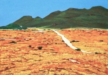 A dirt trail running through a dry, grassy field with green hills in the background and a clear blue sky.