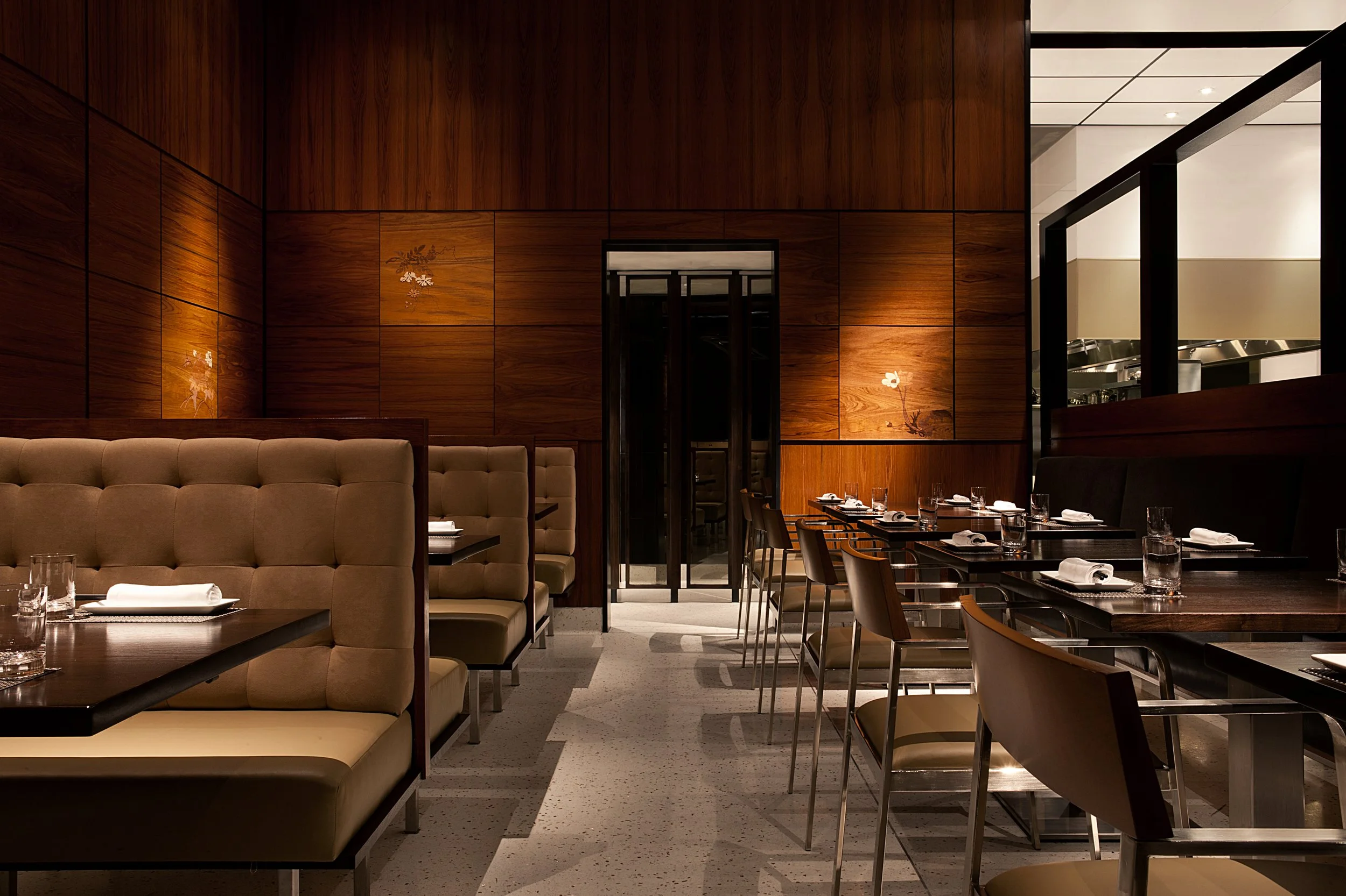 An elegant restaurant interior with dark wood walls, seating booths, and tables set for dining.