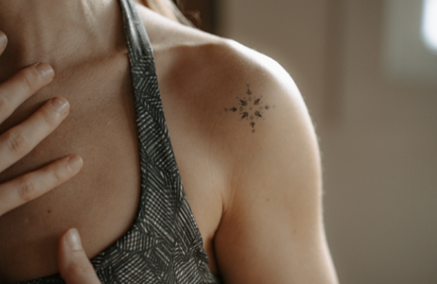 Close-up of a woman's shoulder with a small starburst tattoo and hand touching her chest