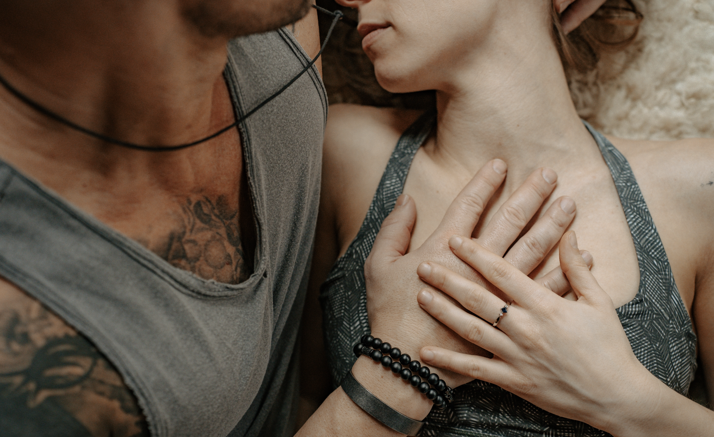 Close-up of a couple embracing, with the woman wearing a ring and the man showing tattoos and bracelets.