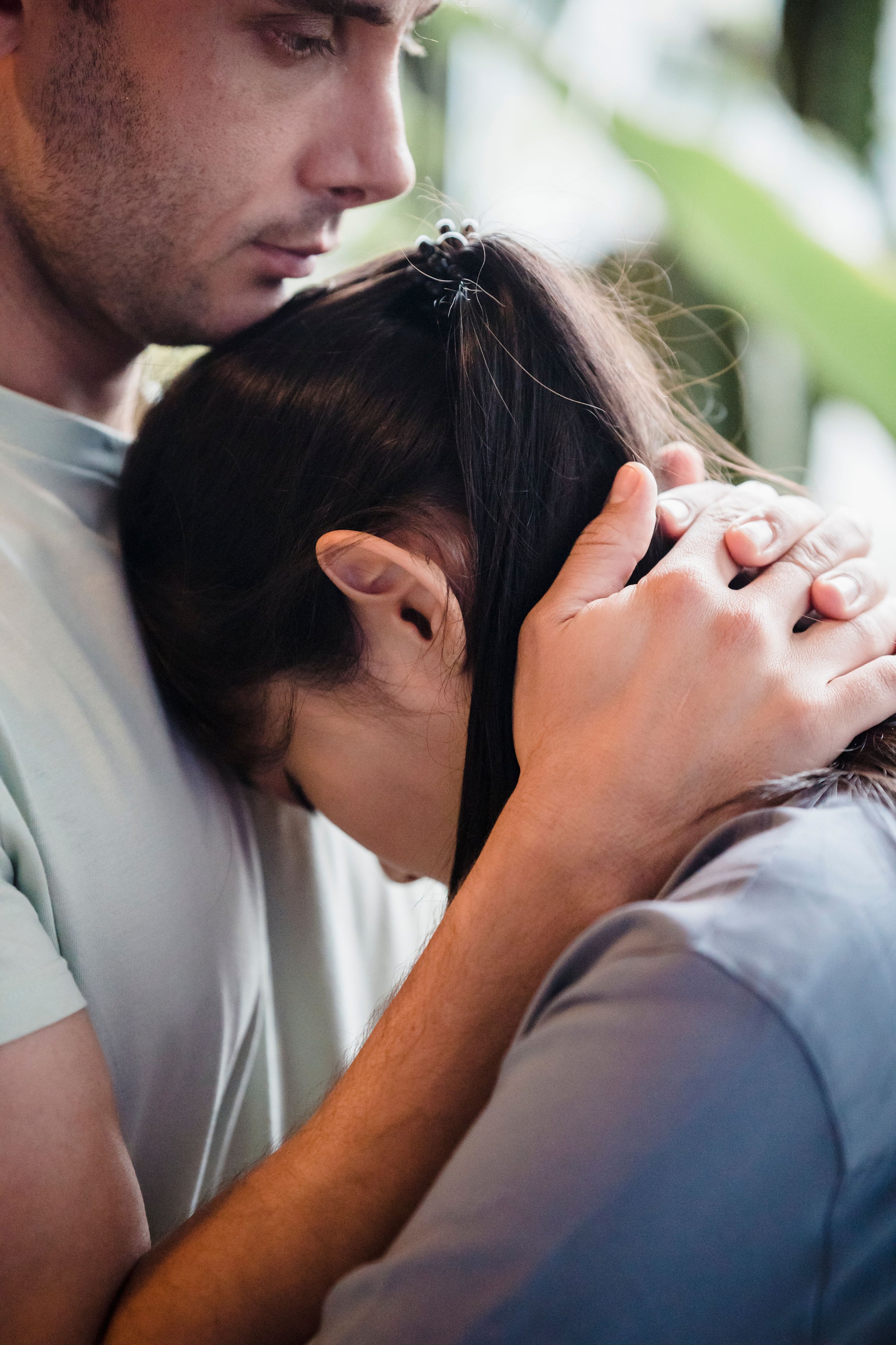 Close-up of a couple embracing, with the man kissing the woman's head outdoors.