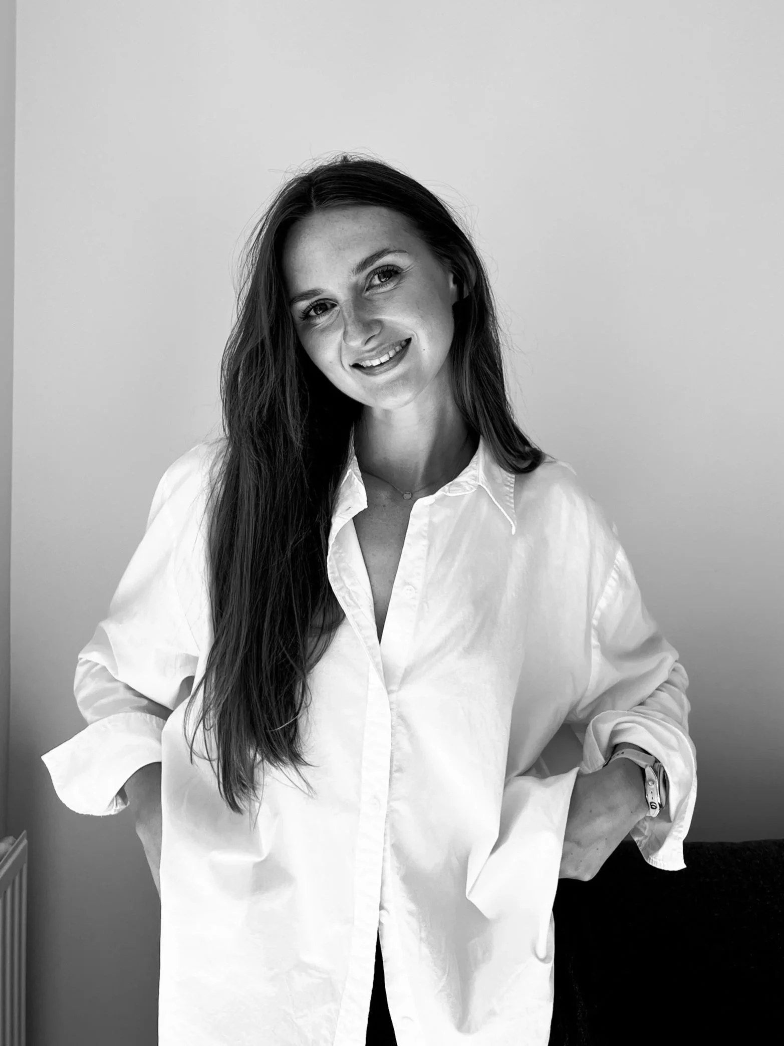 Black and white photograph of a smiling woman with long dark hair, wearing a white shirt, in front of a plain background.
