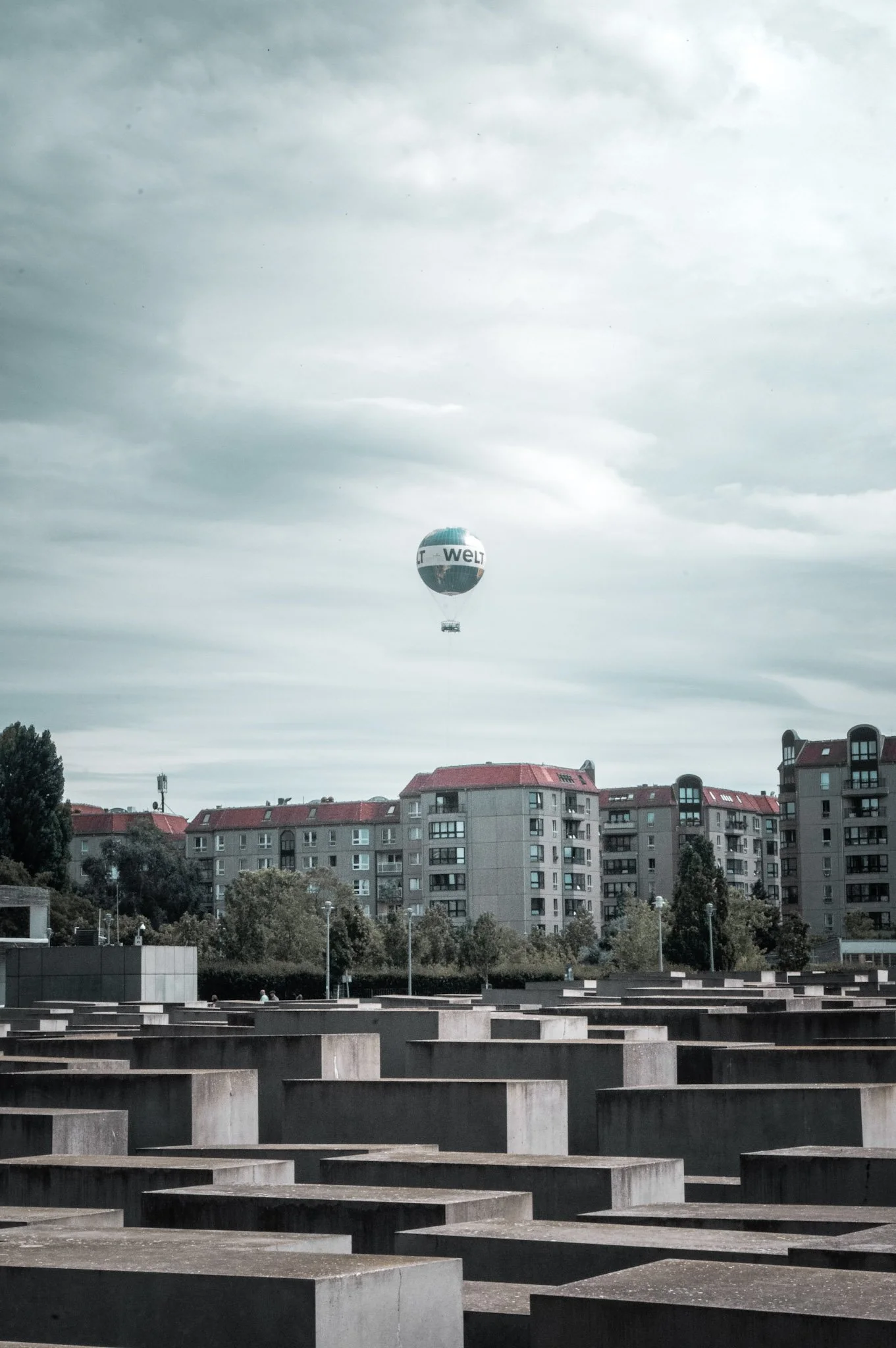 A hot air balloon flying over residential buildings with red rooftops beneath a cloudy sky.
