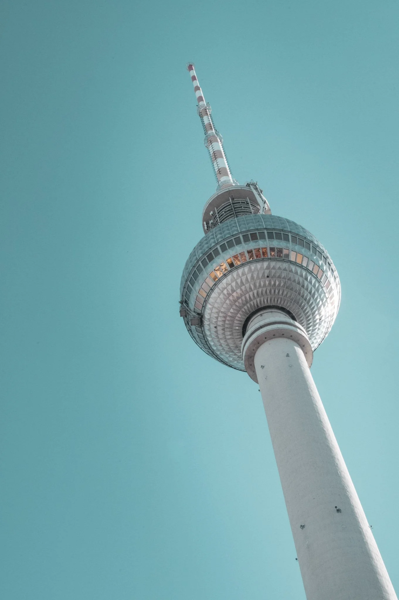 Looking up at a tall communication tower with a spherical observation deck near the top, set against a clear blue sky.