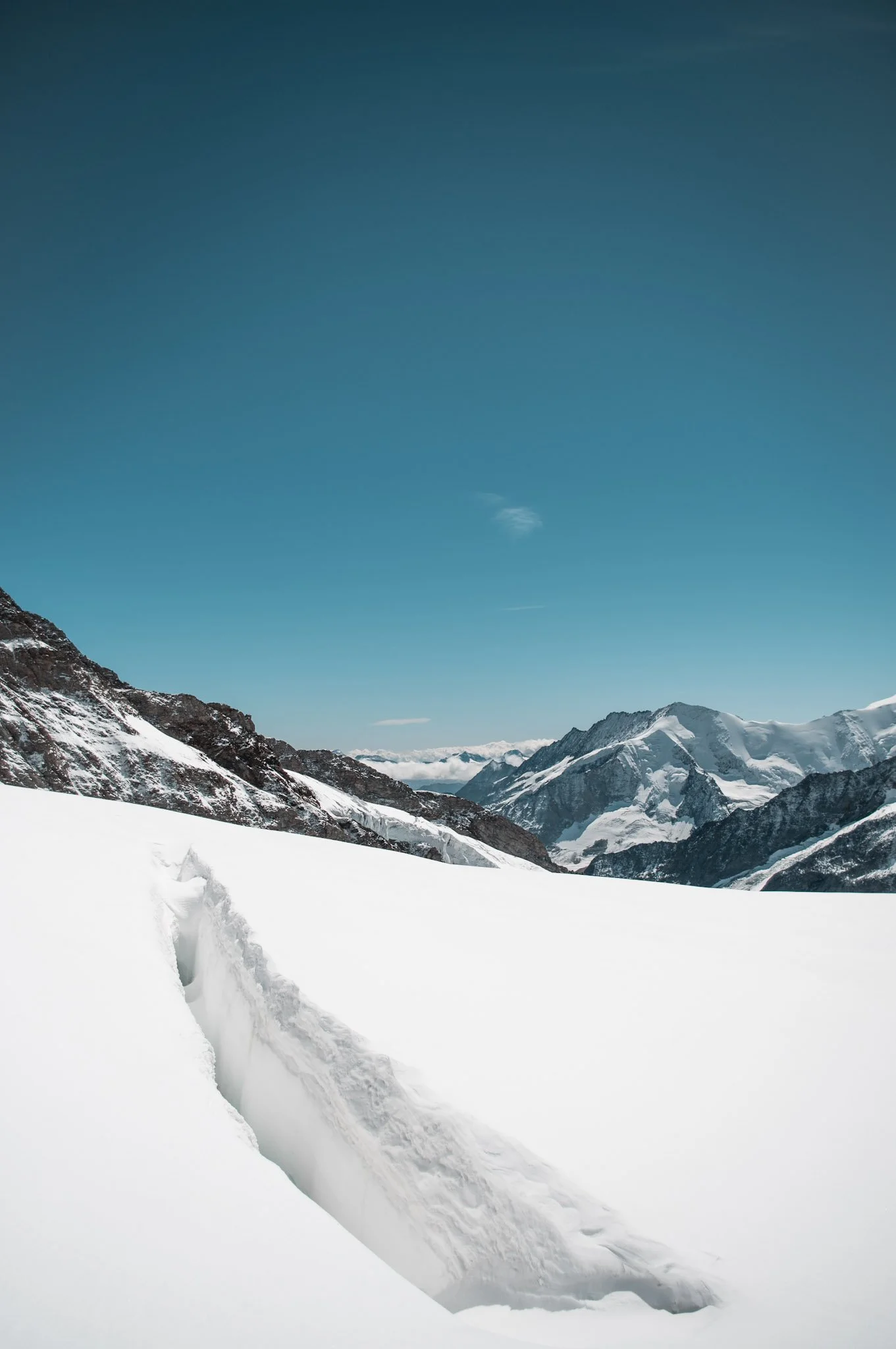 Snow-covered mountain landscape with a sky above and grazing of glaciers and rugged peaks in the distance.