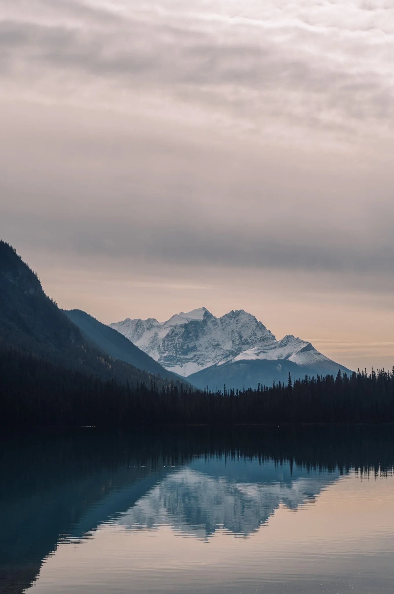Snow-capped mountains reflected in a calm lake with an overcast sky.