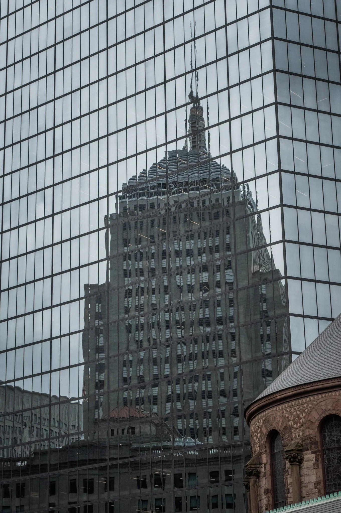Reflection of a historic tower on the glass facade of a modern office building.