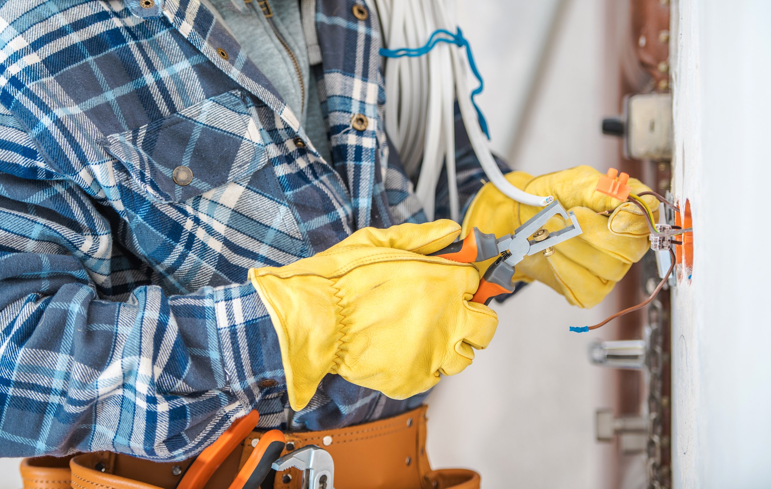 Person wearing yellow gloves working on electrical wiring with pliers in a workshop.