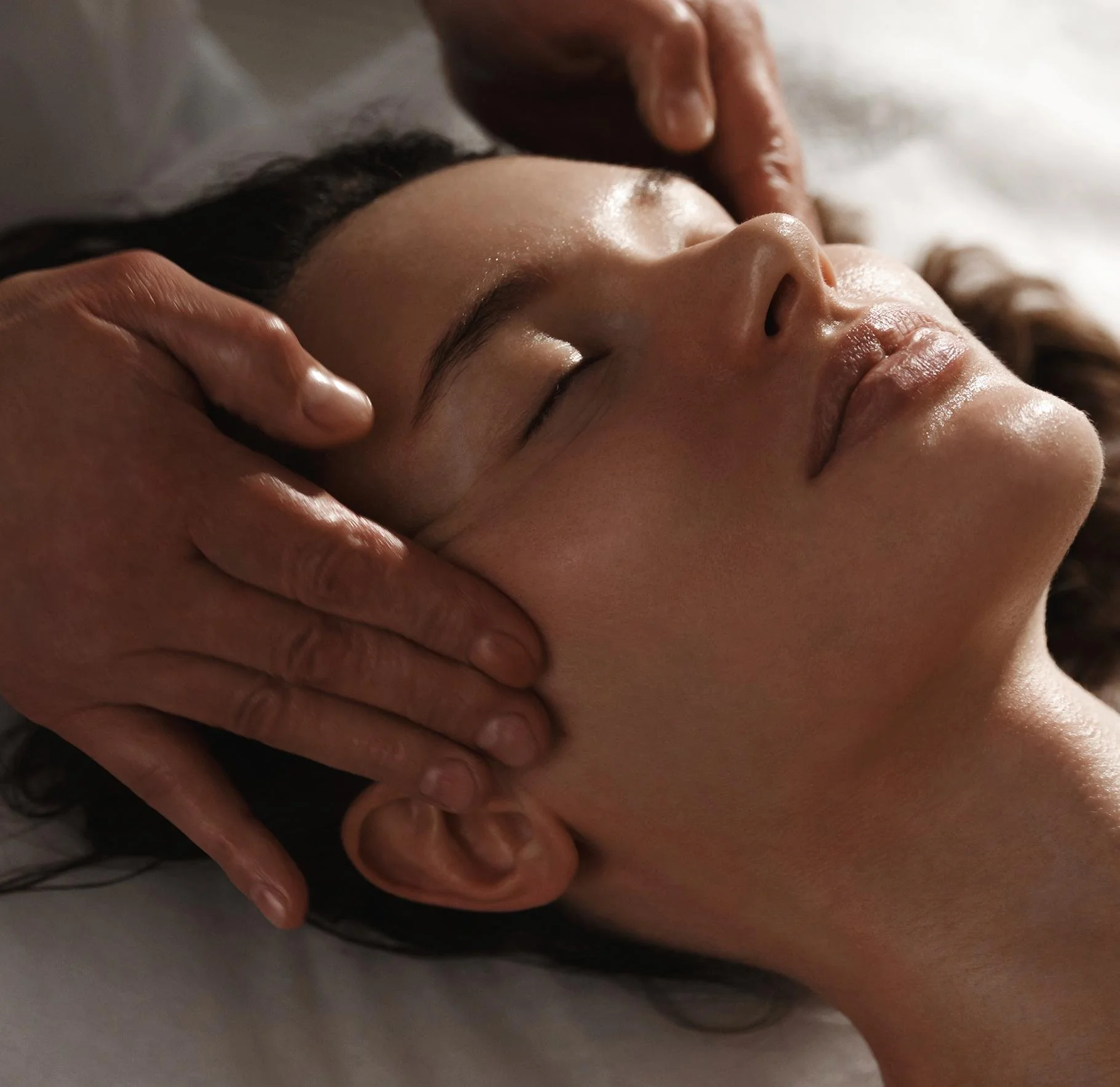 Close-up of a person receiving a facial massage, with the person's face relaxed and eyes closed.