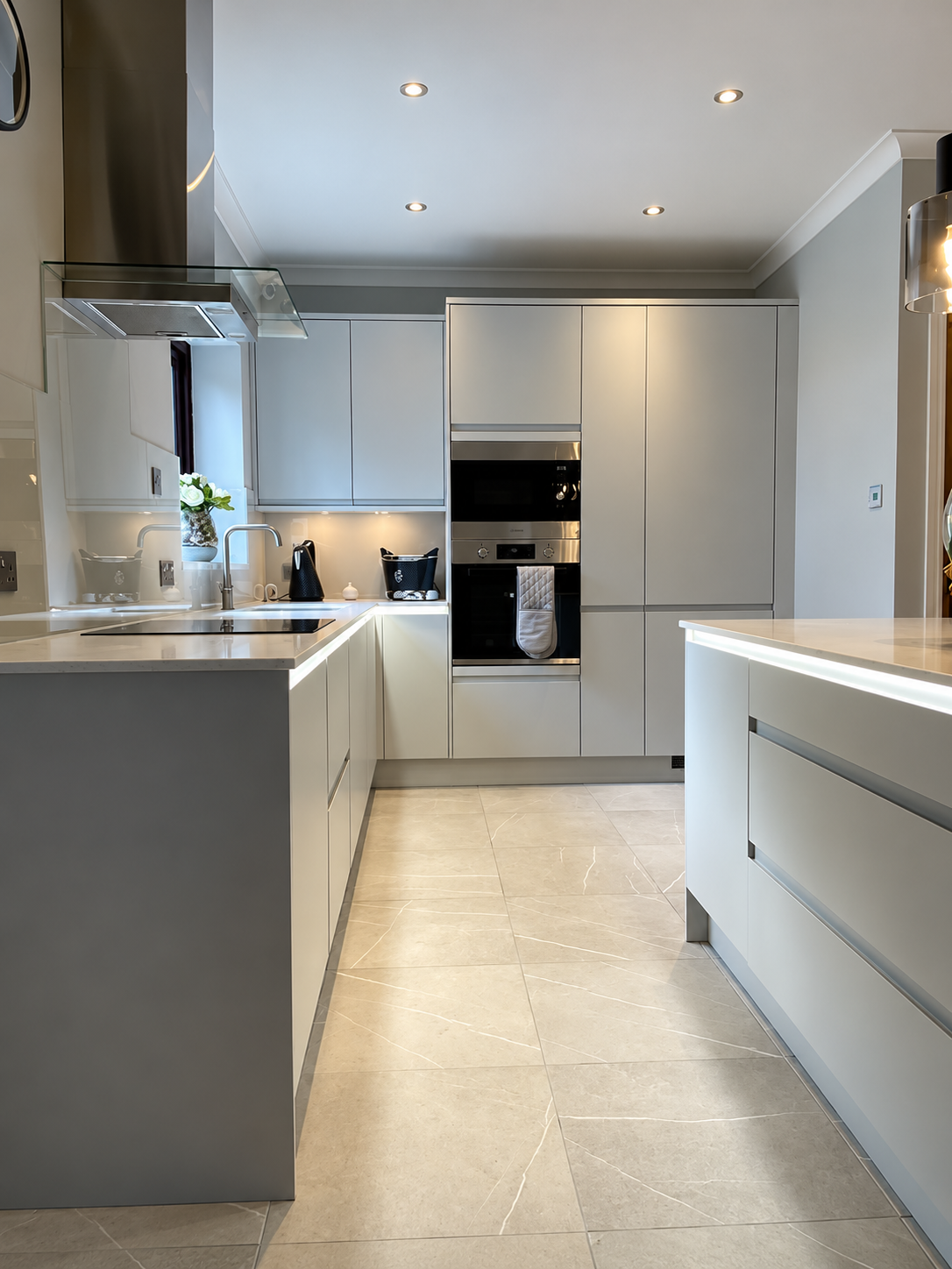 Contemporary kitchen renovation by Oliver Francis Interiors featuring sleek handleless cabinetry, integrated appliances, light stone-effect flooring and modern kitchen island.