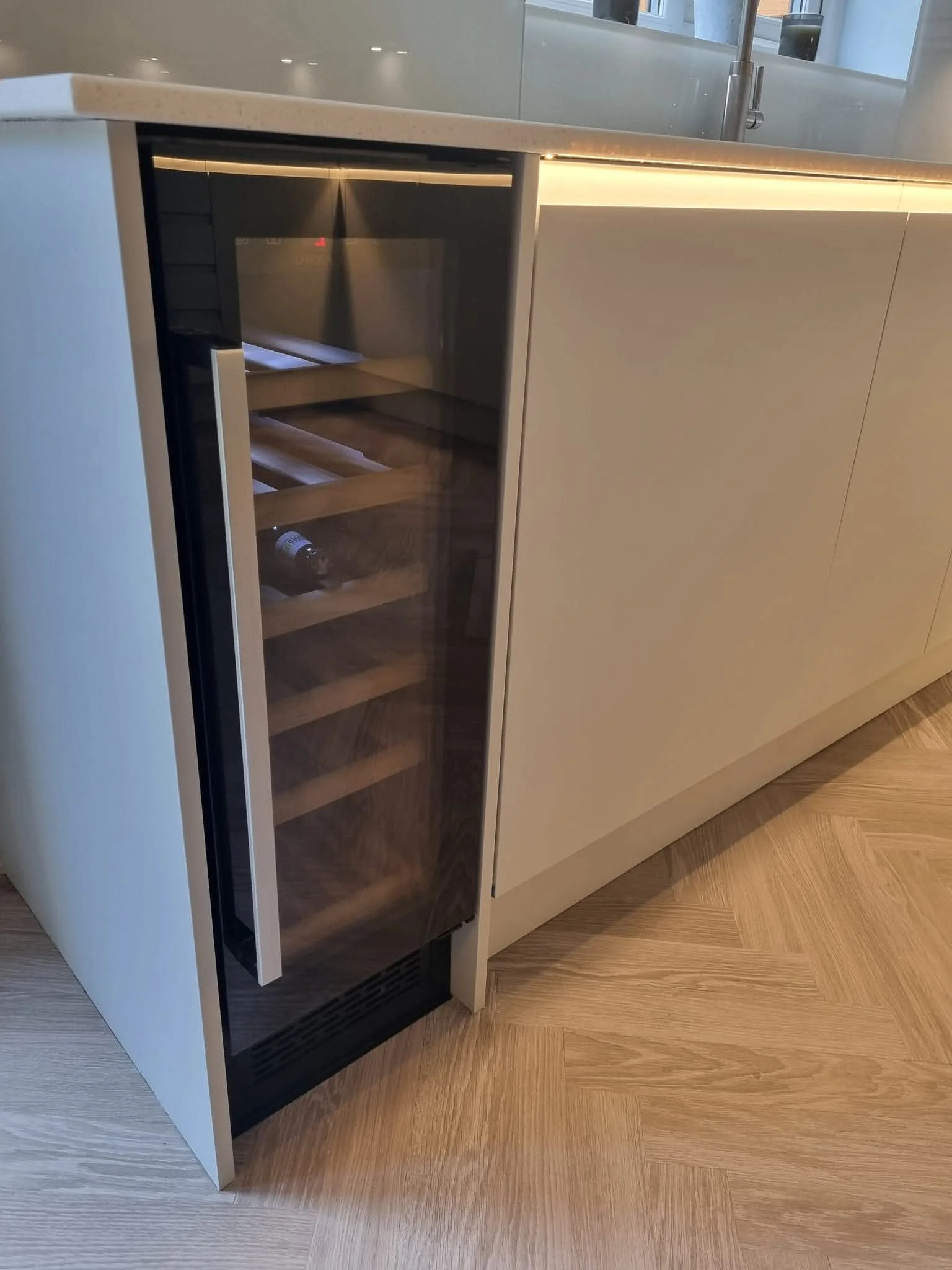 Built-in wine cooler beneath a sleek kitchen worktop, surrounded by contemporary handleless cabinetry.
