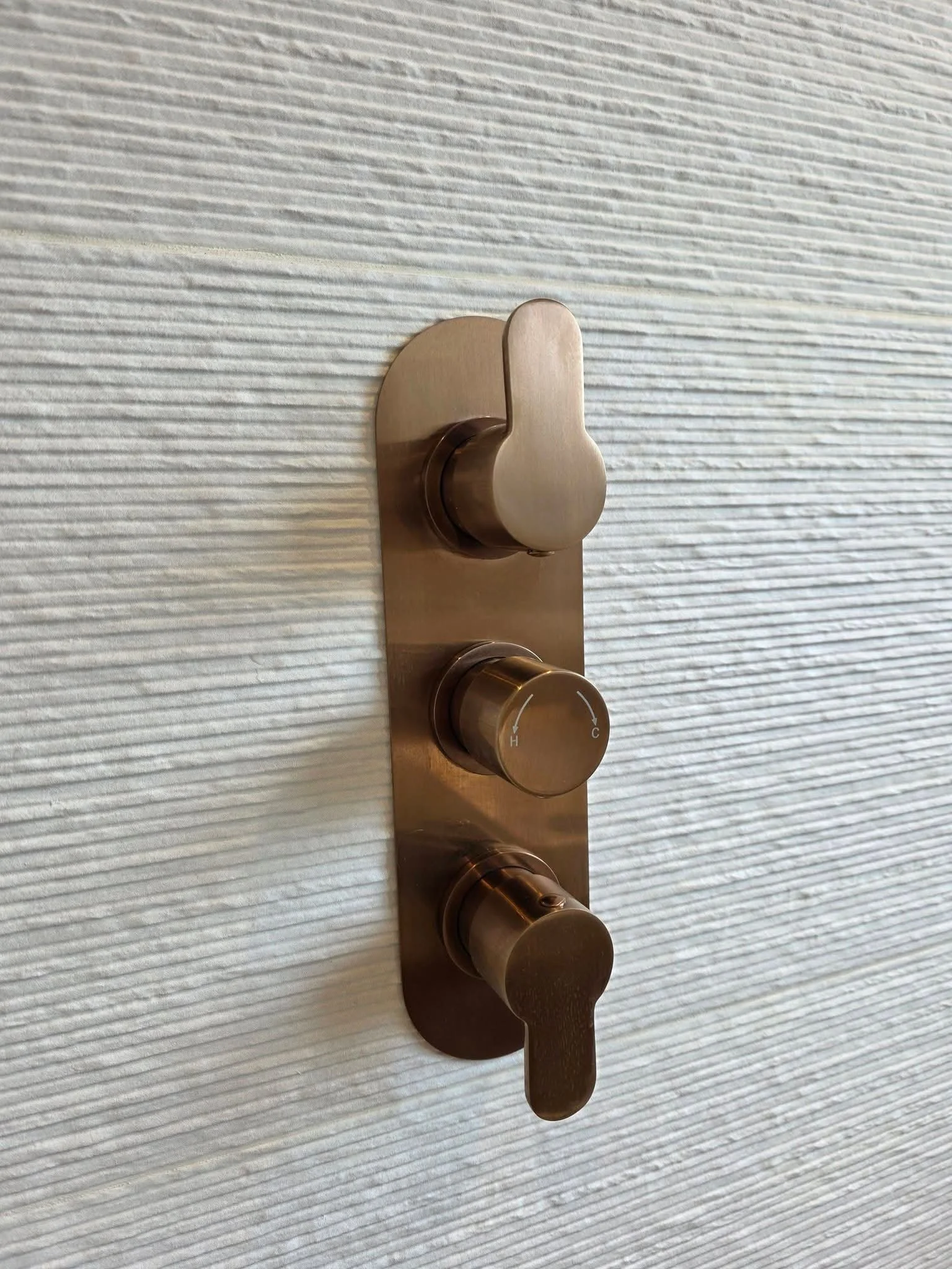 Brushed bronze shower controls fitted against textured tiles in a bathroom renovation in Hadfield by Oliver Francis Interiors.
