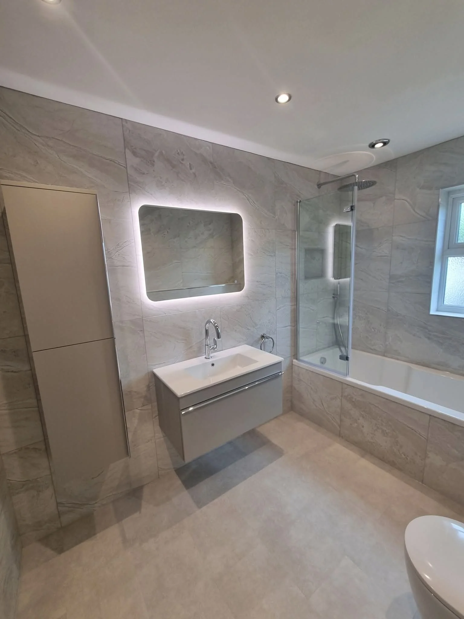 A complete bathroom renovation in Hayfield, creating a bright, contemporary space with large-format tiling, a wall-hung vanity and bath with overhead shower.