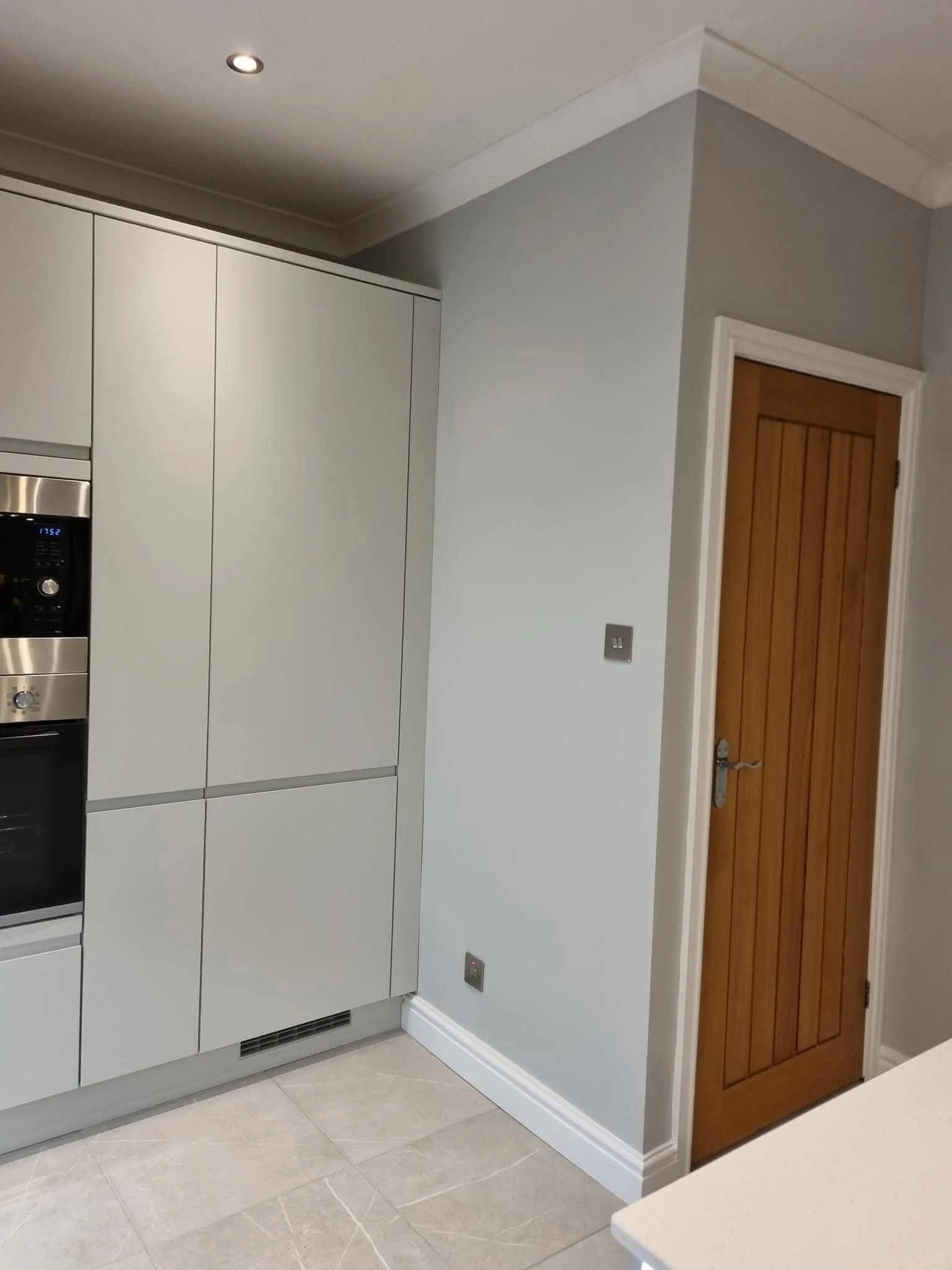 Floor-to-ceiling handleless kitchen cabinetry with integrated oven, light stone-effect flooring and modern finishing touches.