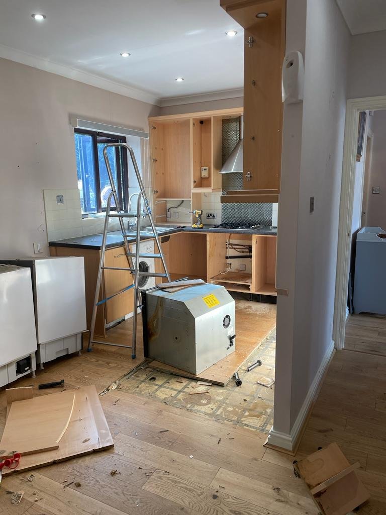 Kitchen under renovation with removed cabinets, tools, ladder, and construction materials on the floor.
