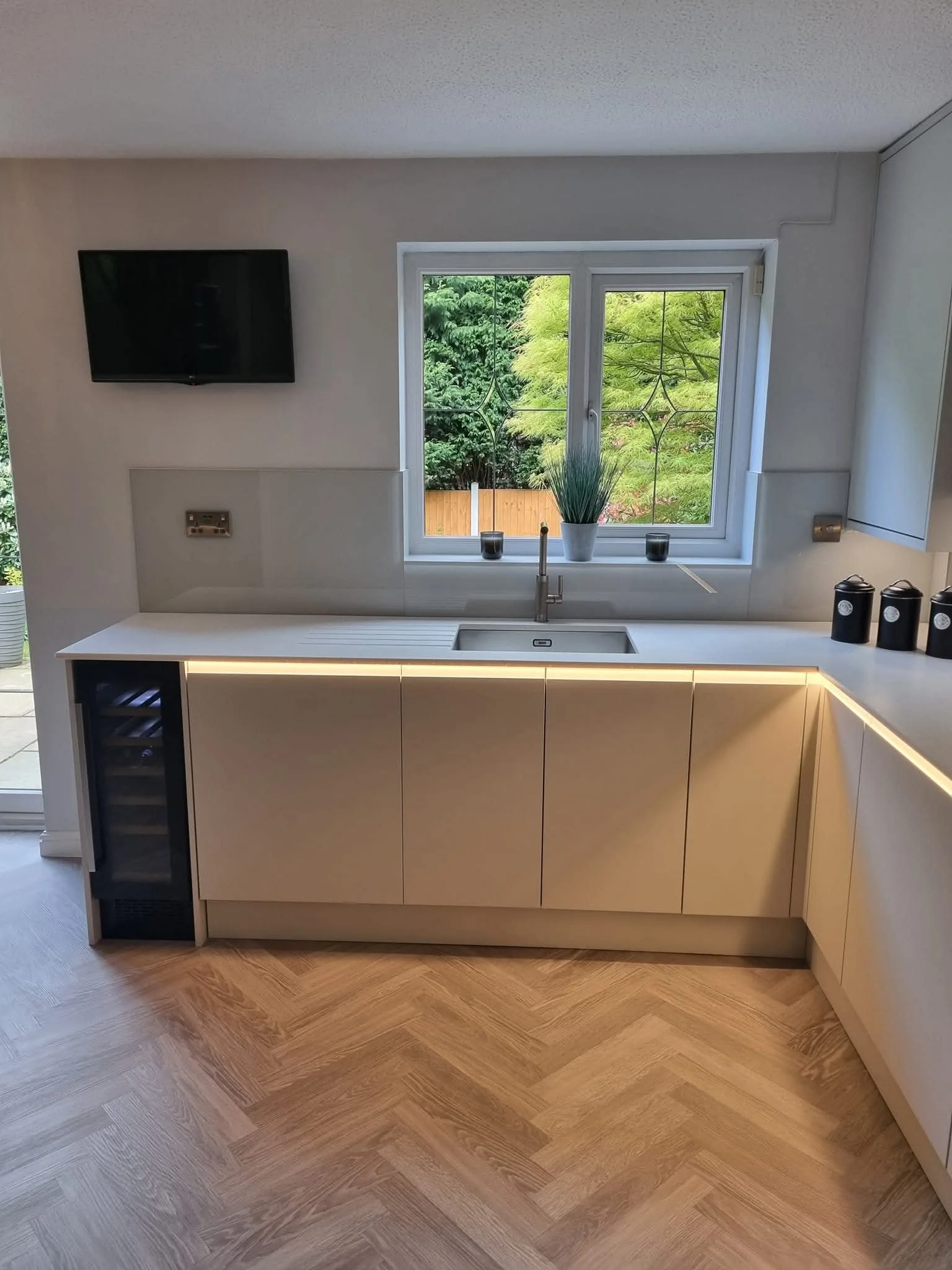 Modern kitchen renovation by Oliver Francis Interiors featuring dove-grey handleless cabinets, an integrated wine cooler, undermount sink, LED lighting and herringbone flooring.