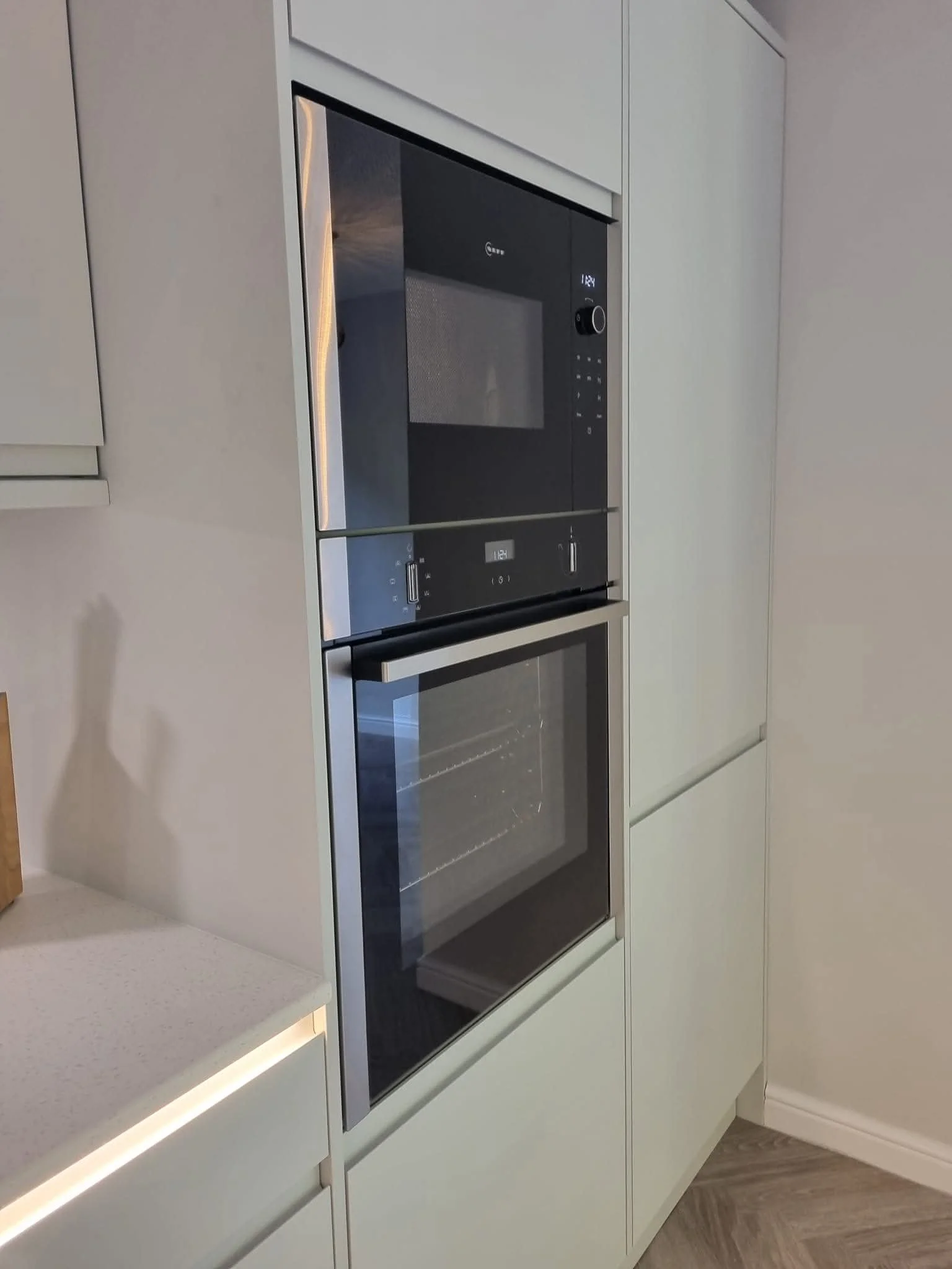 Built-in black glass ovens integrated into contemporary dove-grey kitchen cabinetry by Oliver Francis Interiors.
