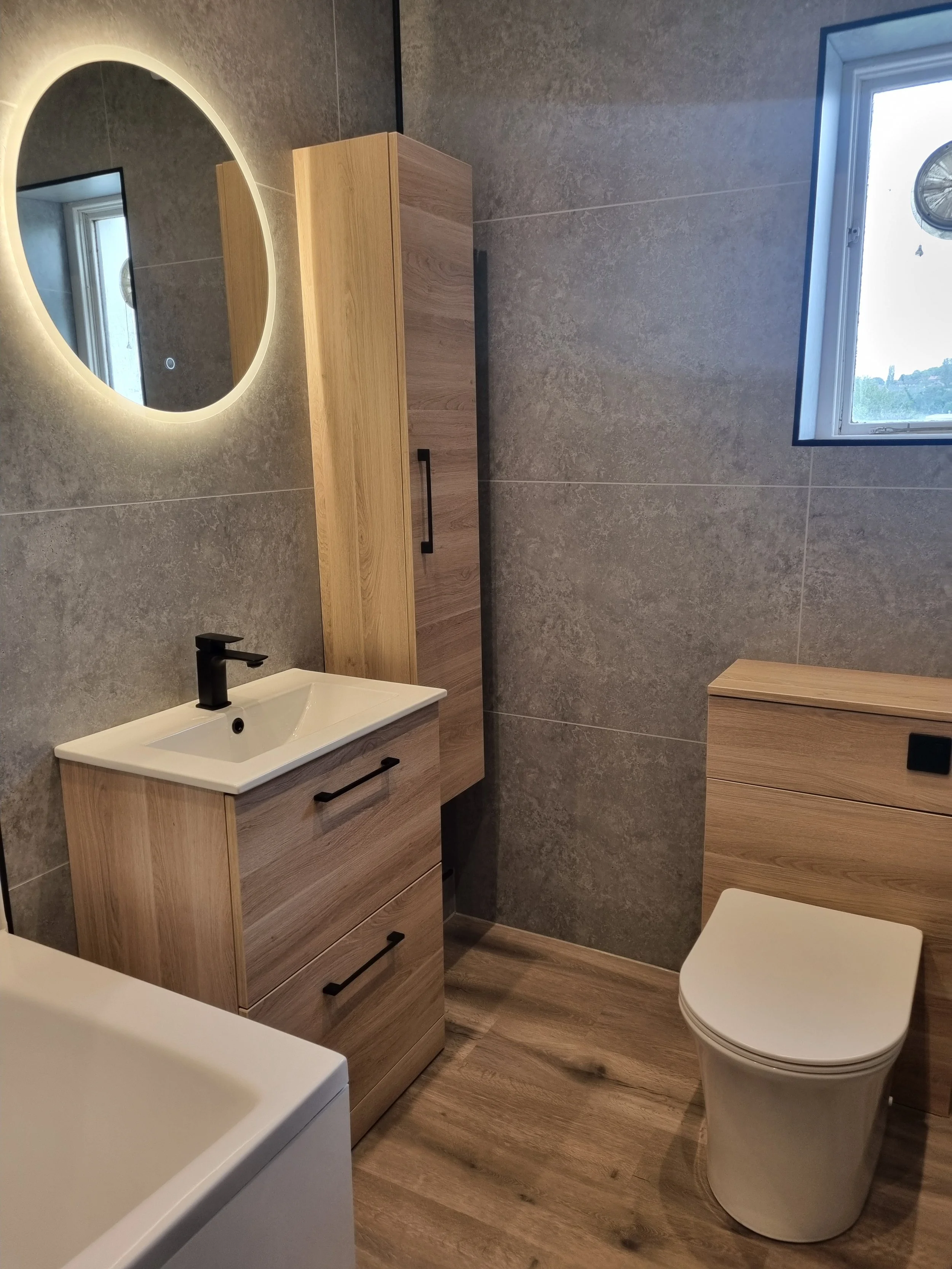 Contemporary bathroom renovation by Oliver Francis Interiors featuring grey wall tiles, oak-effect vanity furniture, black fittings and modern sanitaryware.