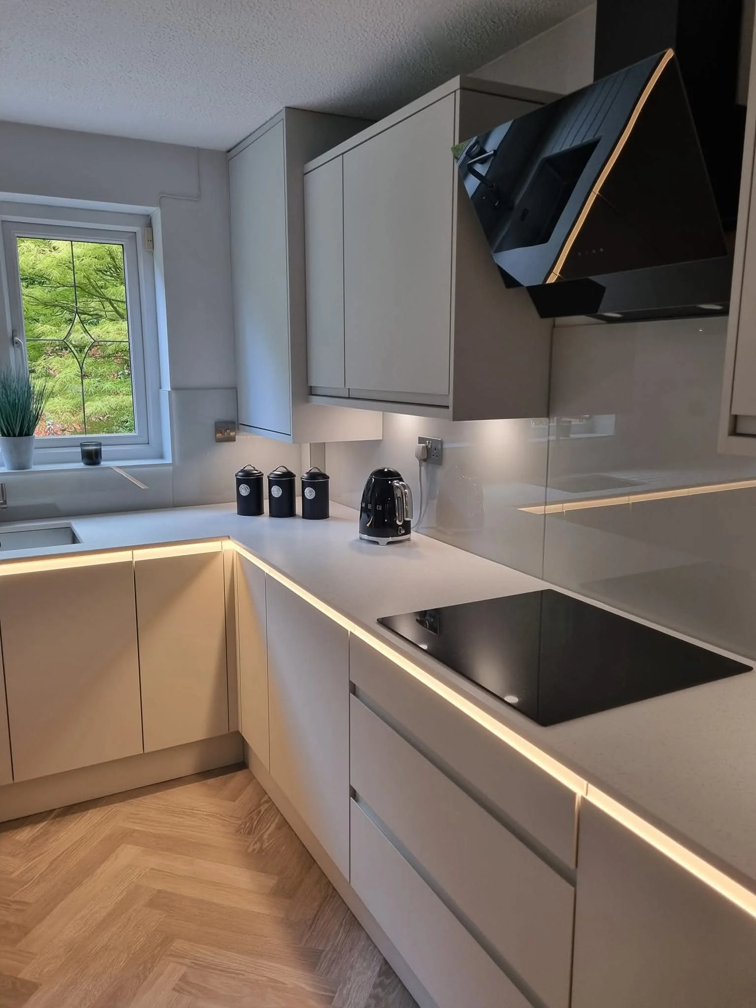 Contemporary kitchen renovation featuring matt dove-grey handleless cabinets, integrated lighting and herringbone-effect flooring.
