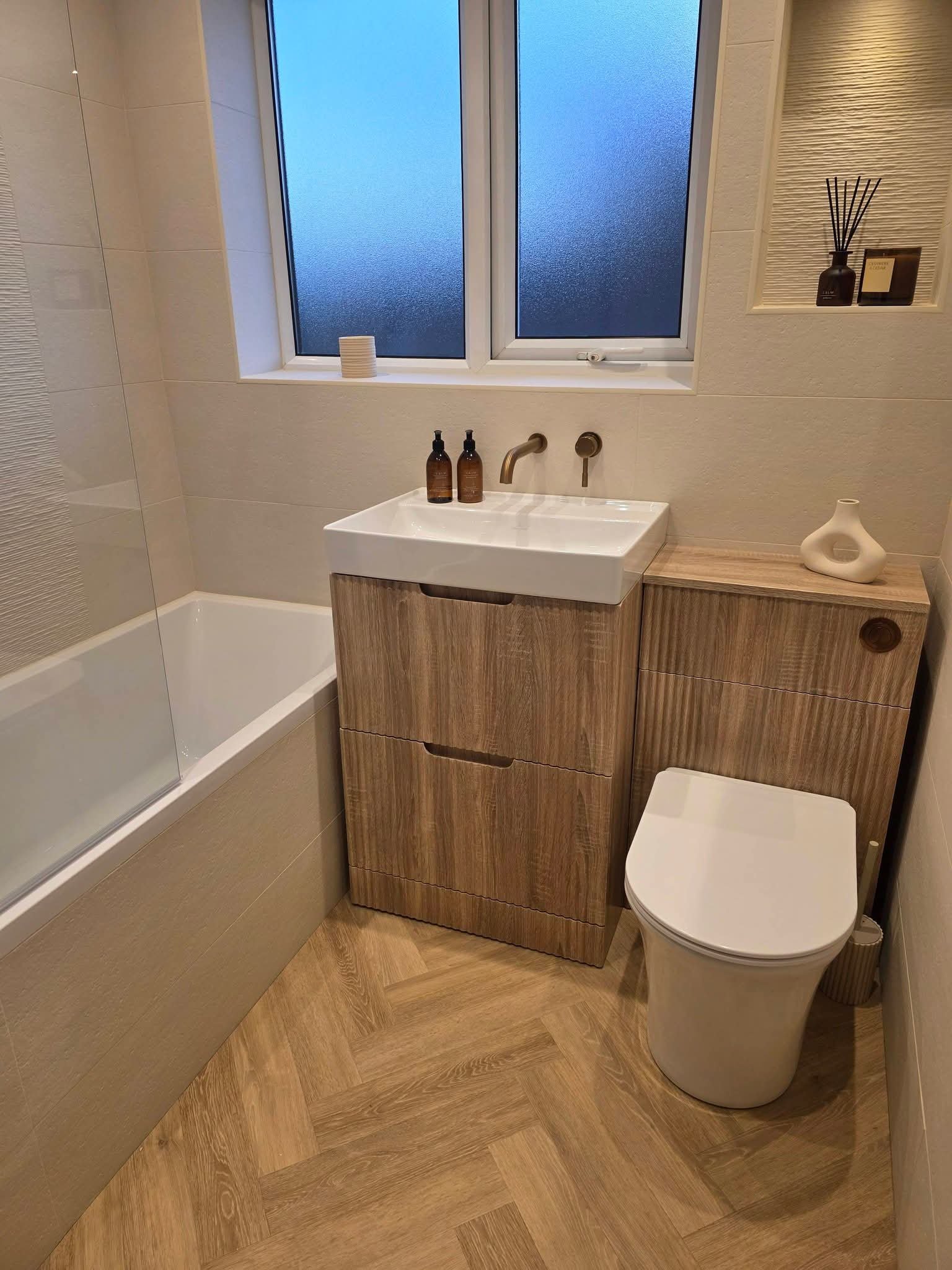 Modern family bathroom renovation in Hadfield, Glossop featuring a fitted bathtub, wood-effect vanity unit, countertop basin, white toilet and warm neutral finishes.