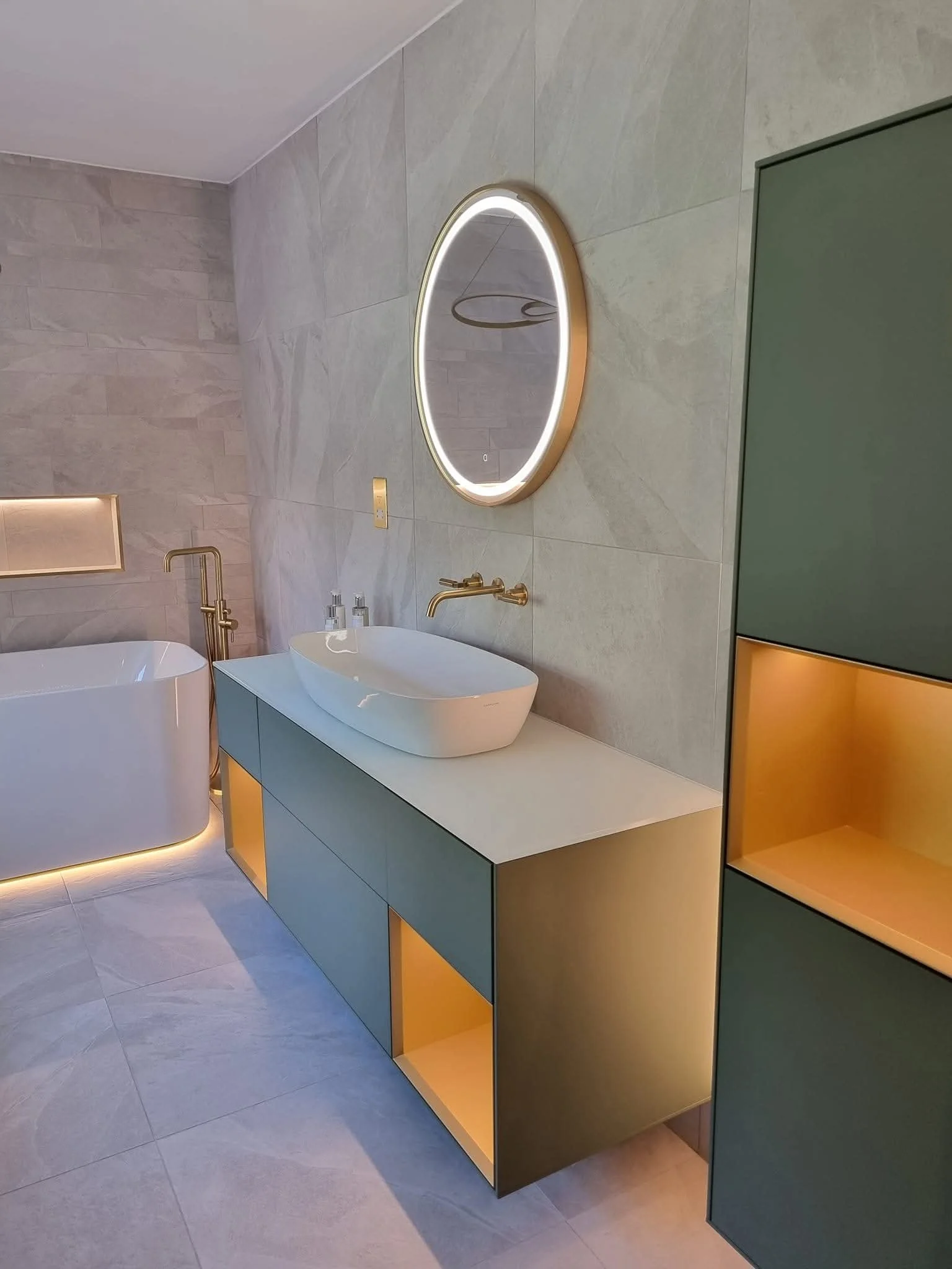 Contemporary bathroom renovation featuring a colourful vanity unit, round illuminated mirror, countertop basin and brushed gold fittings.