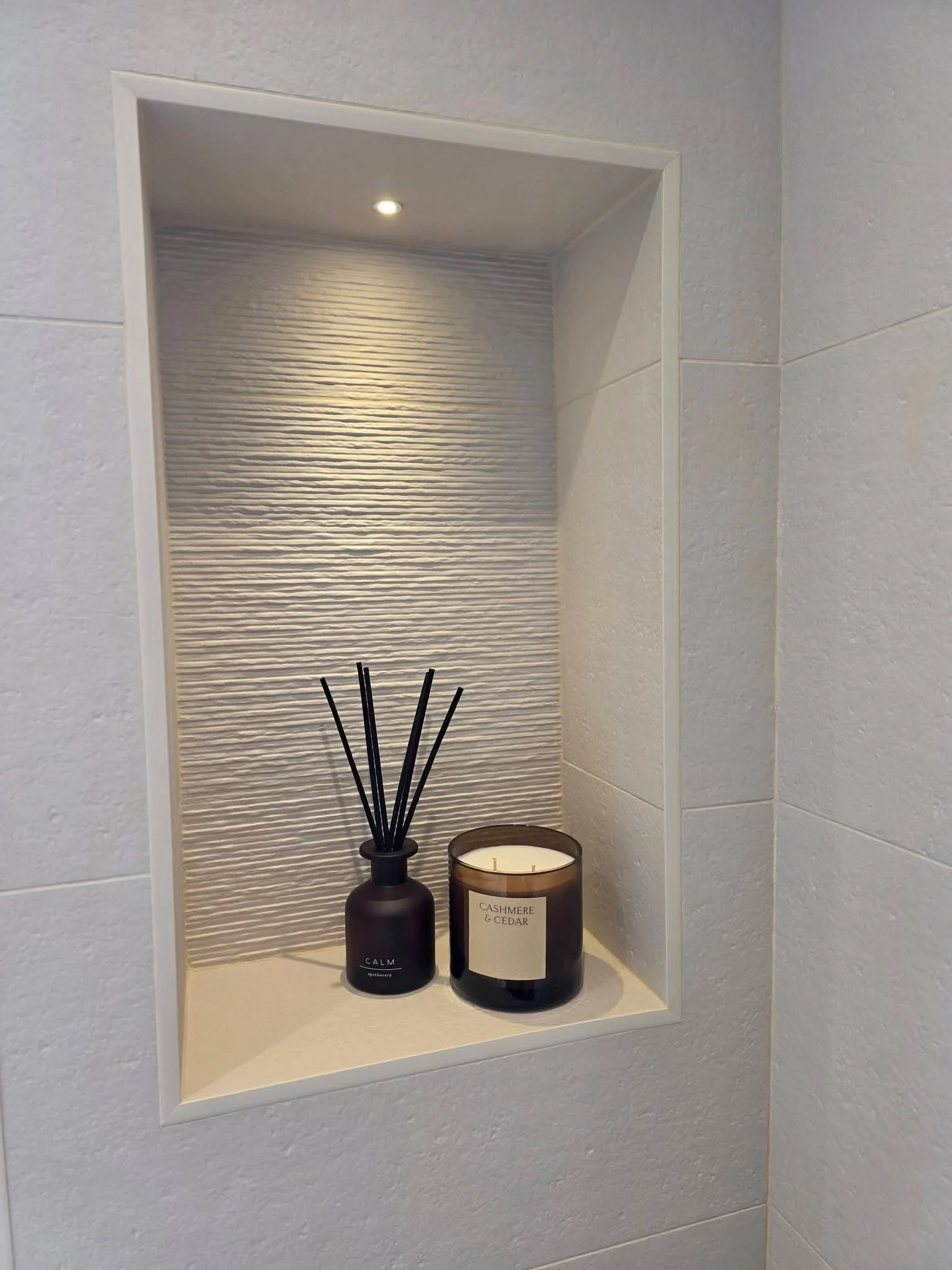 Recessed bathroom wall niche in Hadfield, Glossop with integrated lighting, textured tiles and decorative shelving, finished with a candle and reed diffuser.