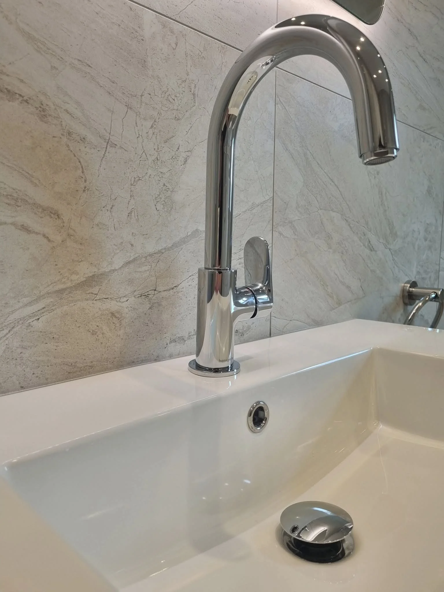 Close-up of white bathroom basin with chrome mixer tap and light stone-effect wall tiles.