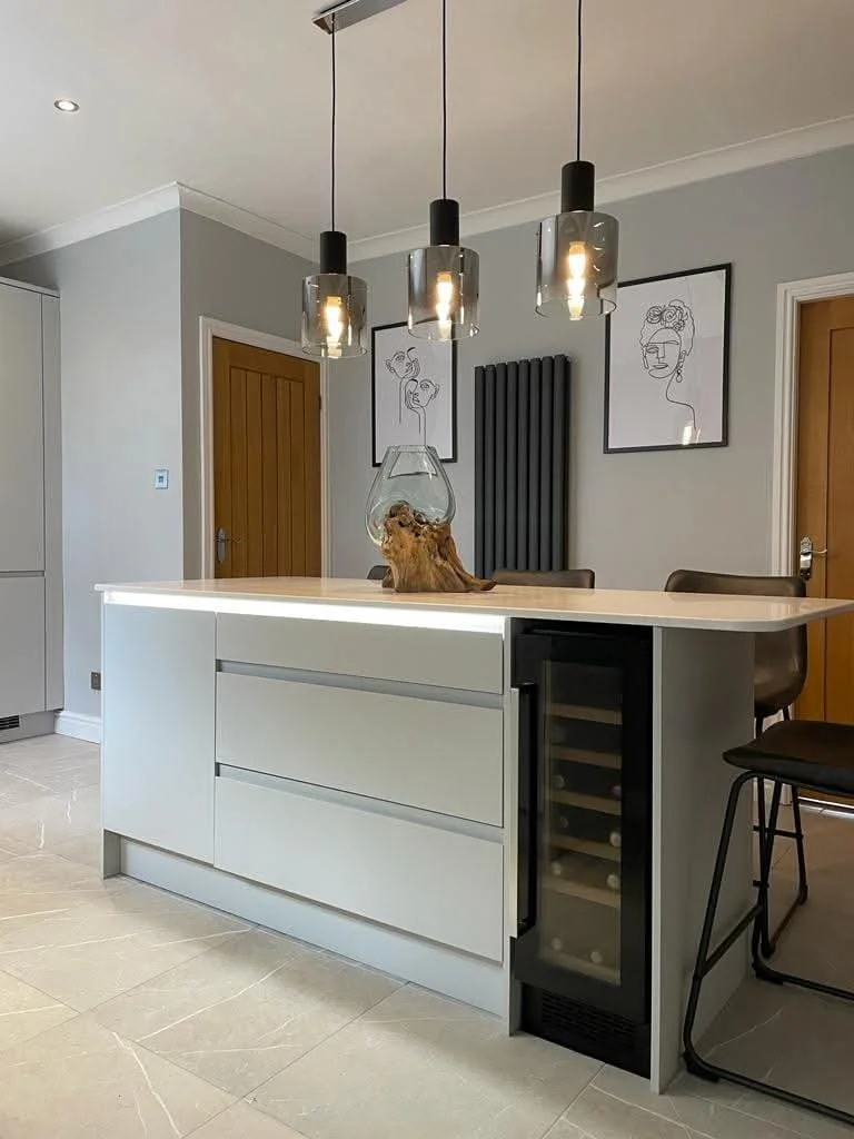 Modern kitchen renovation featuring a white breakfast bar, integrated wine cooler, pendant lighting and contemporary cabinetry.